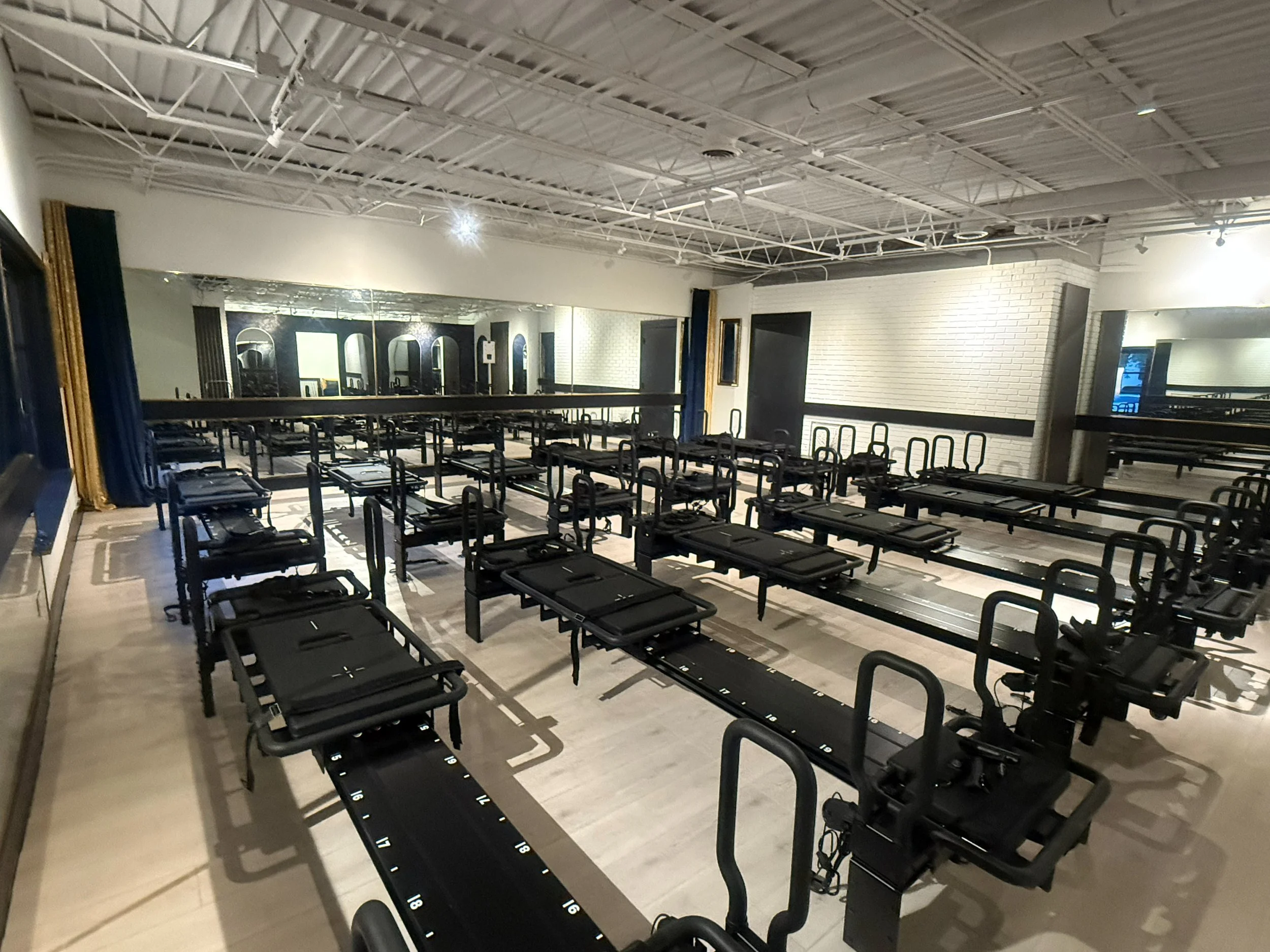 Venom Lagree Wheaton Studio with rows of Lagree machines in a bright studio with white brick, long mirrors and velvet drapes