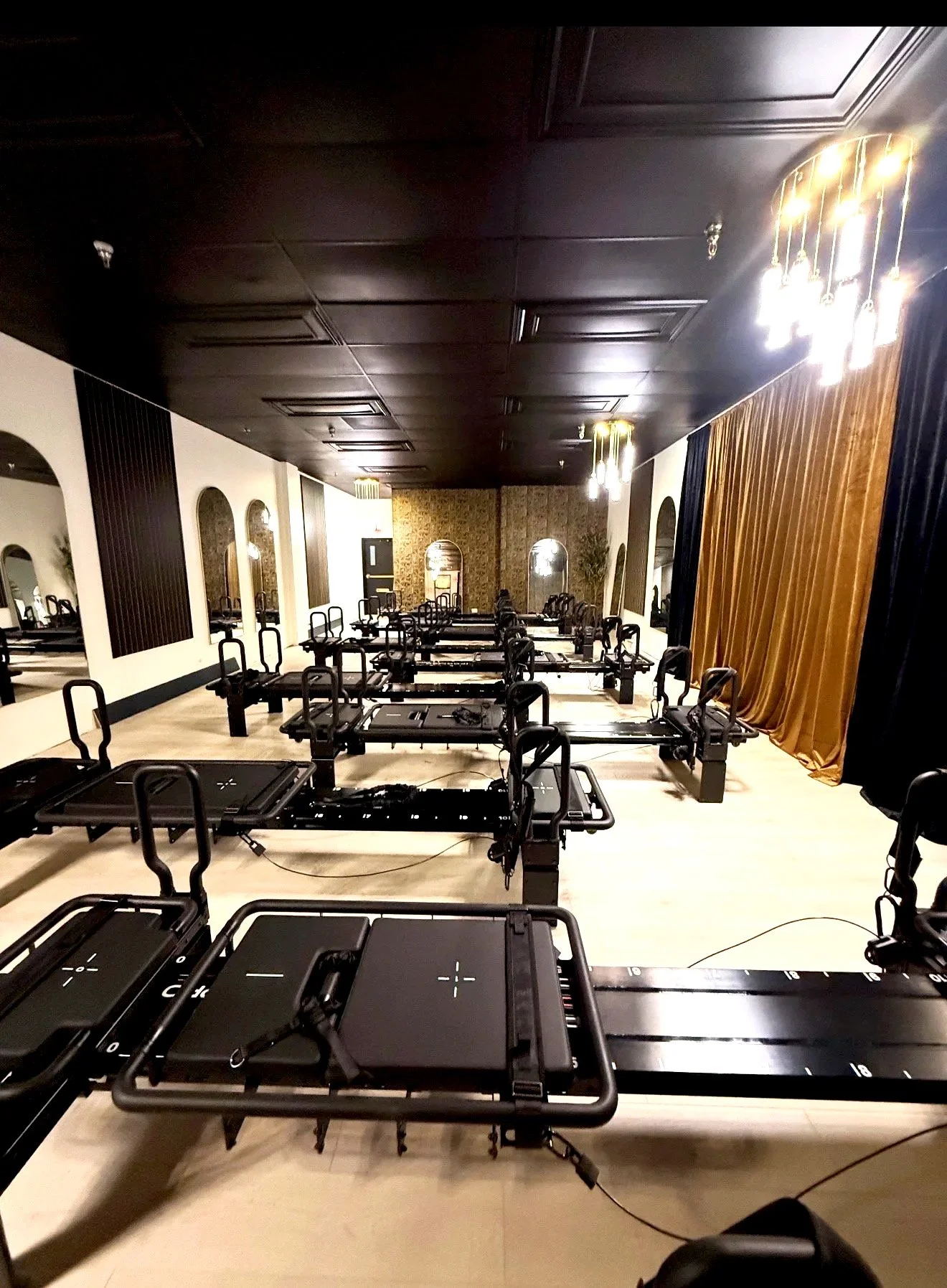 Venom Lagree Naperville studio with a long studio of Lagree machines under a black ceiling, glowing pendant lights and gold drapes