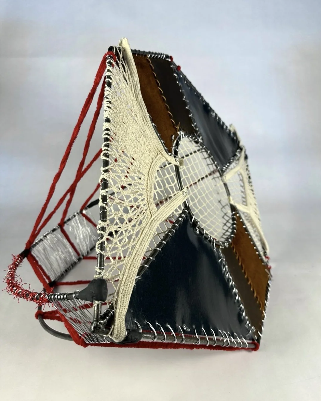 A pyramid-shaped sculpture made of wires, fabrics, and mixed materials with a geometric design.