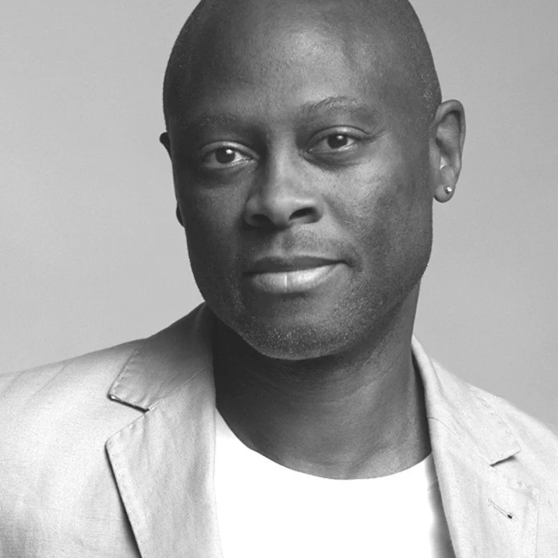 Black man in a light-colored blazer and white shirt, looking at the camera with a slight smile.