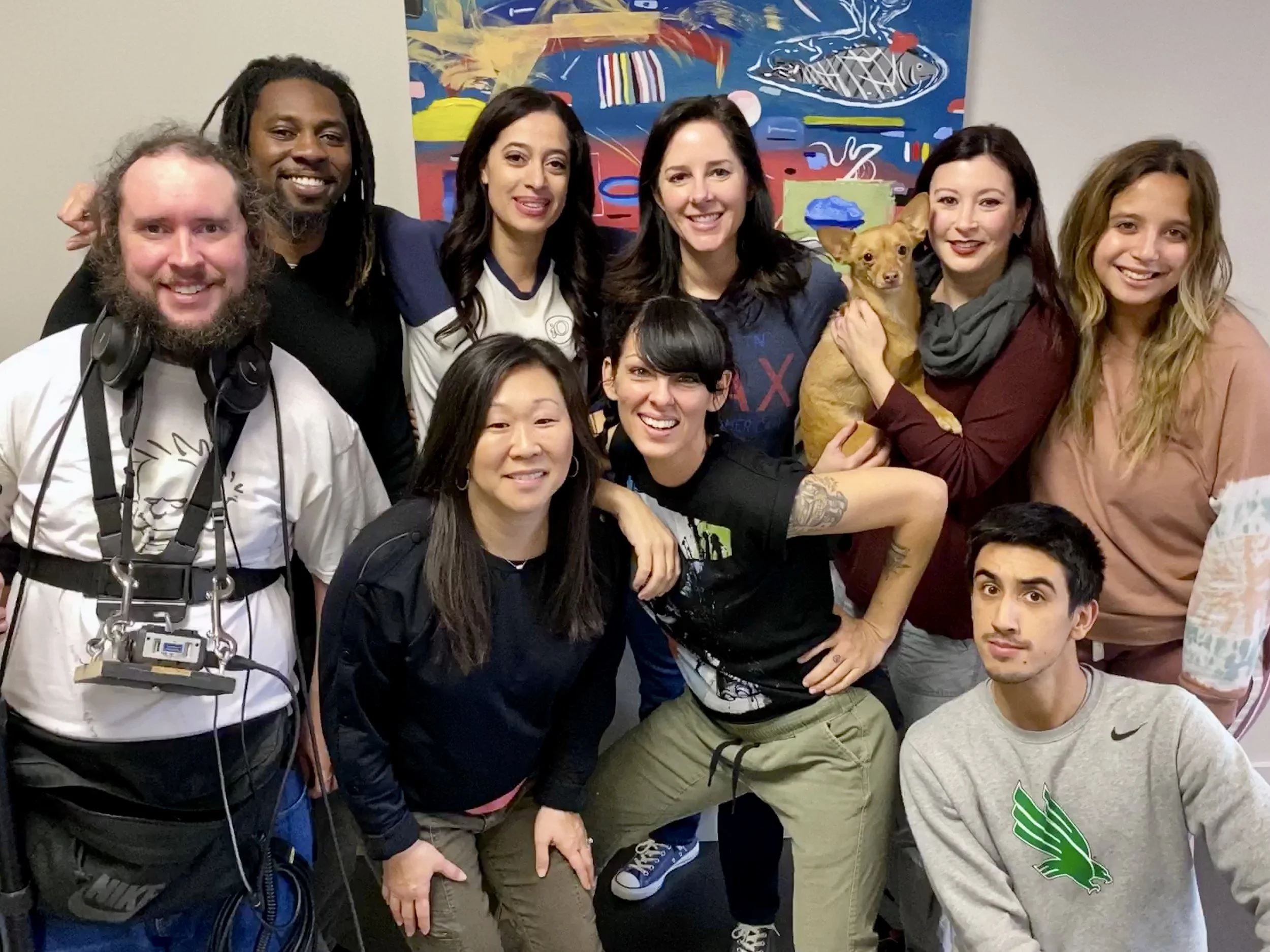Group of eight diverse people and a small dog posing together indoors.
