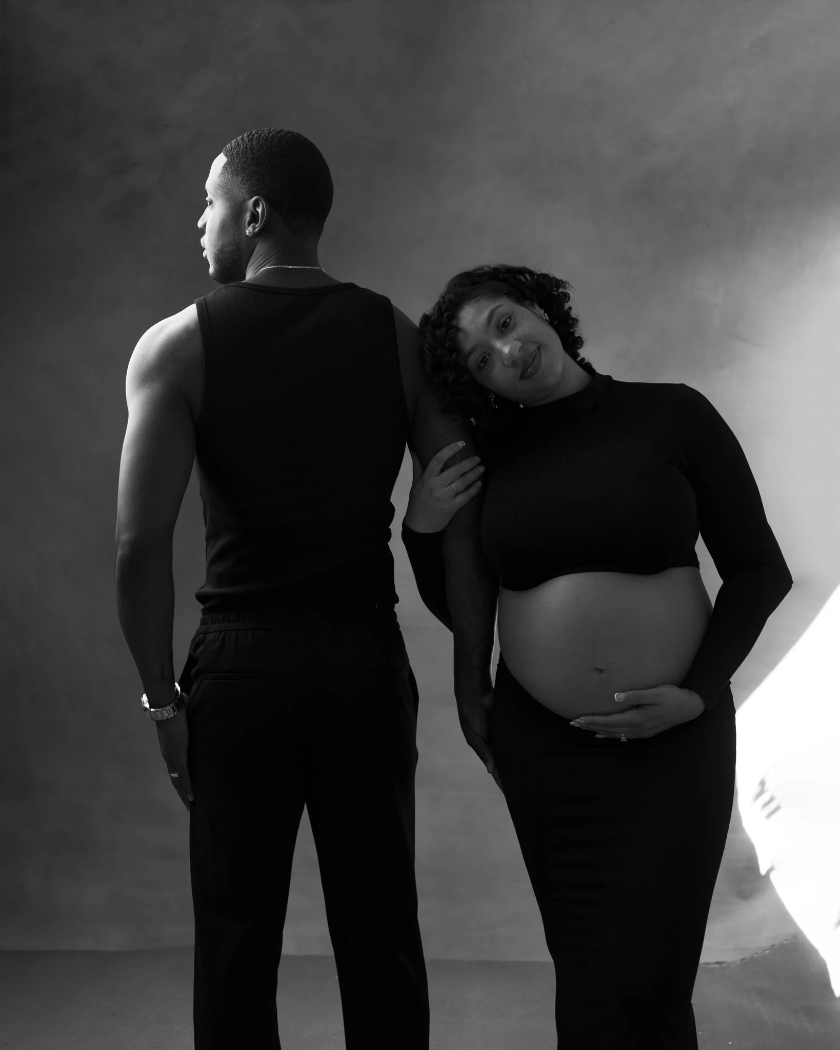 Expectant couple embracing near a sunlit window during an intimate in-home maternity photoshoot.