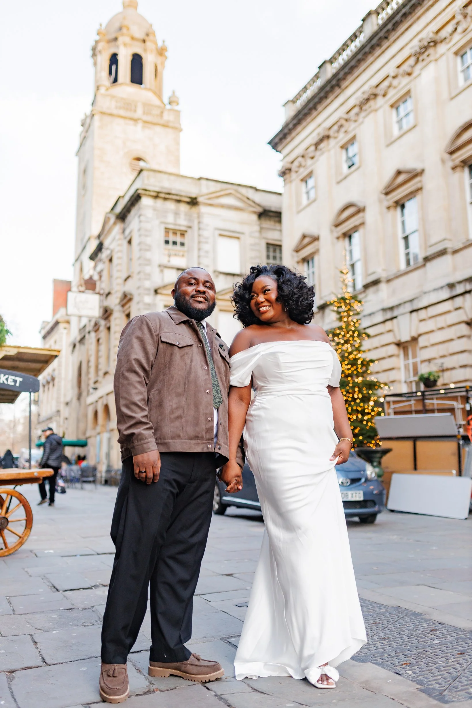Newlywed couple holding hands while walking through central Bristol streets during their post-wedding portrait session.