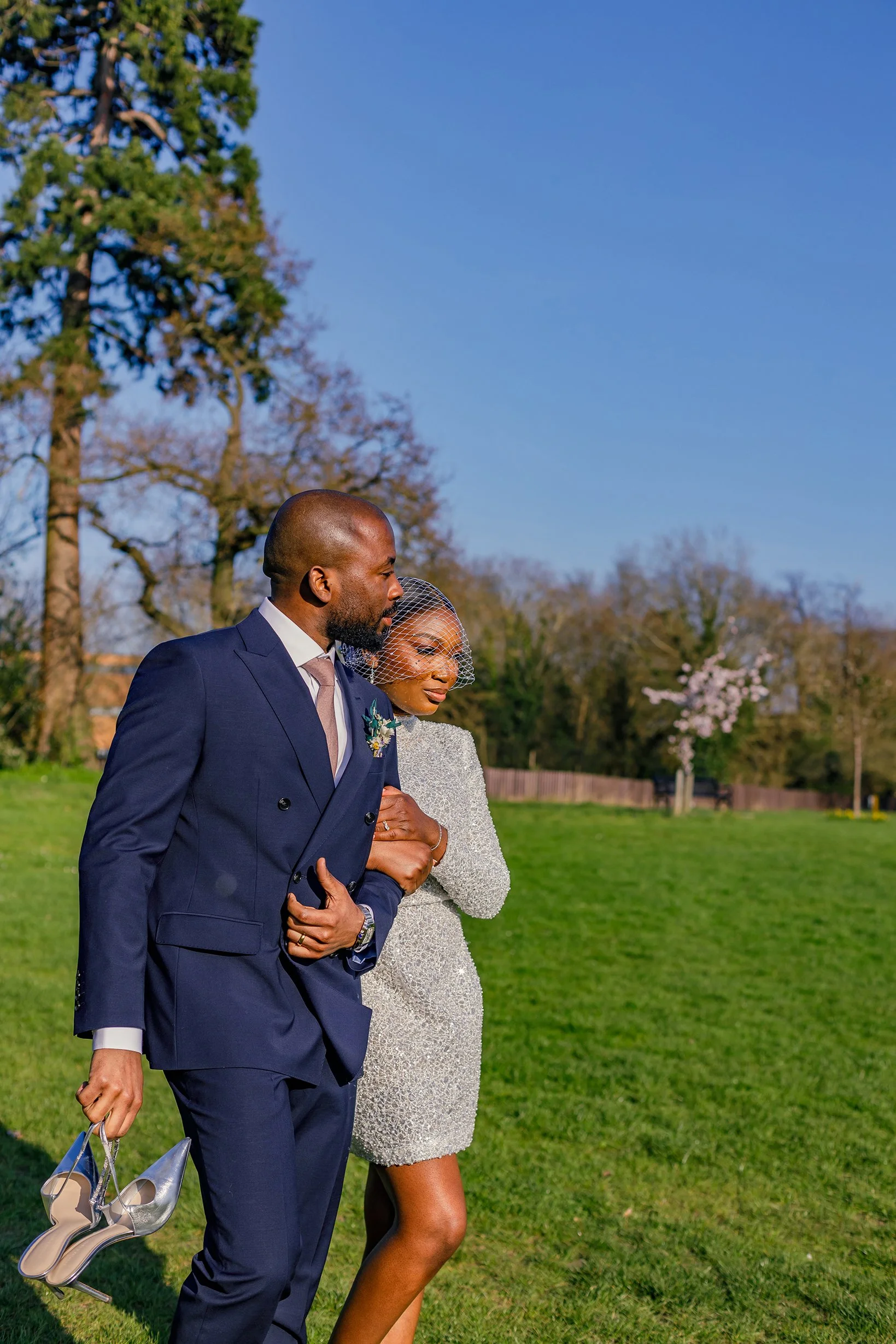 Newlywed couple sharing an intimate embrace while walking on the large lawn behind Merton Register Office in South West London.