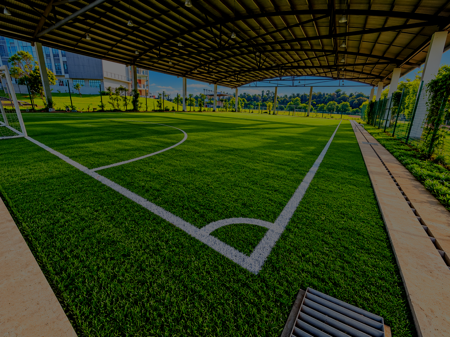 Indoor soccer field with artificial grass, marked lines, and a goal post in an enclosed sports facility with a metal roof and large windows.
