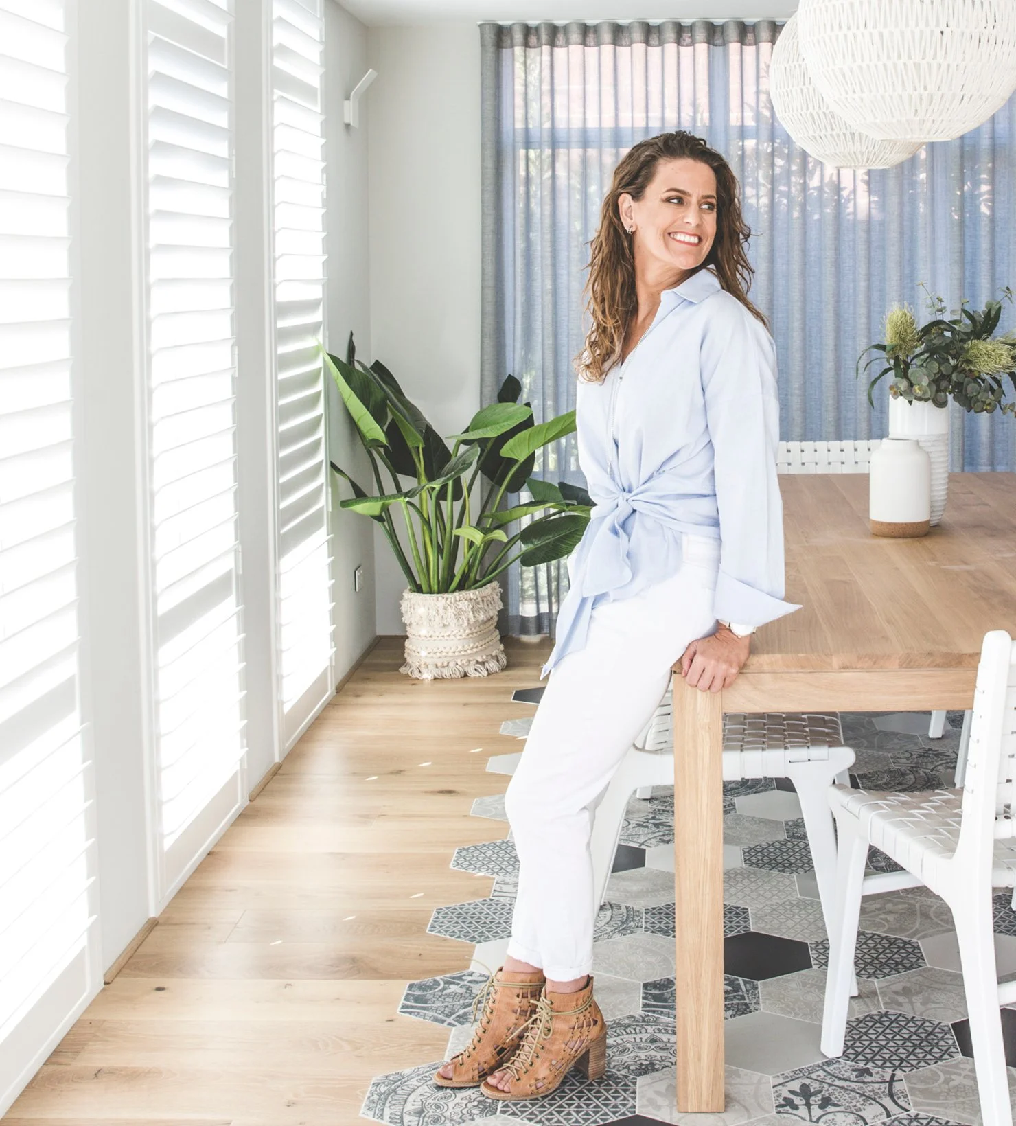 Melissa Redwood beside a timber dining table in a bright room with white shutters and indoor plants