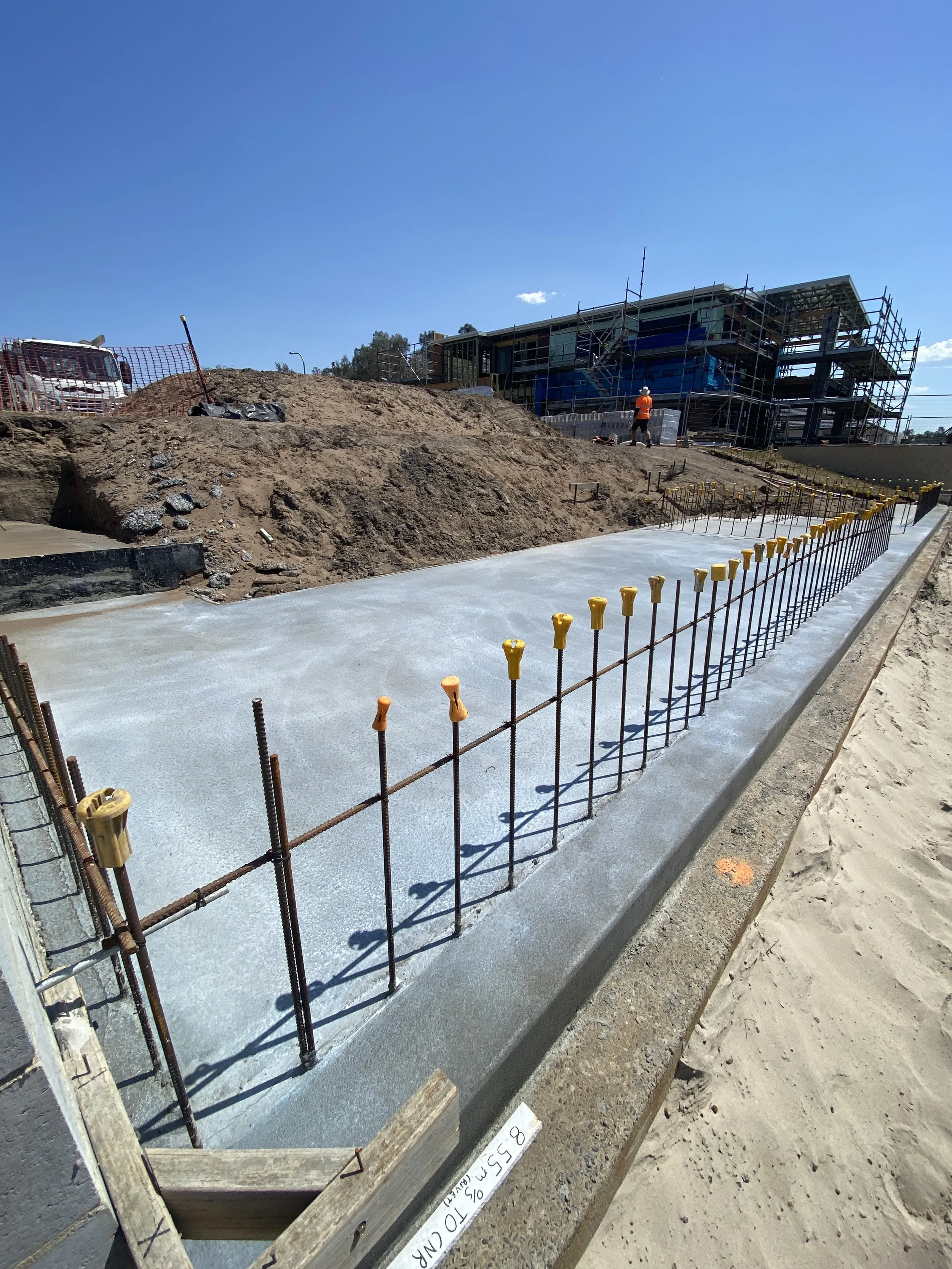 Construction site with a concrete foundation, steel rebar, and workers building a multi-story building under a clear blue sky.