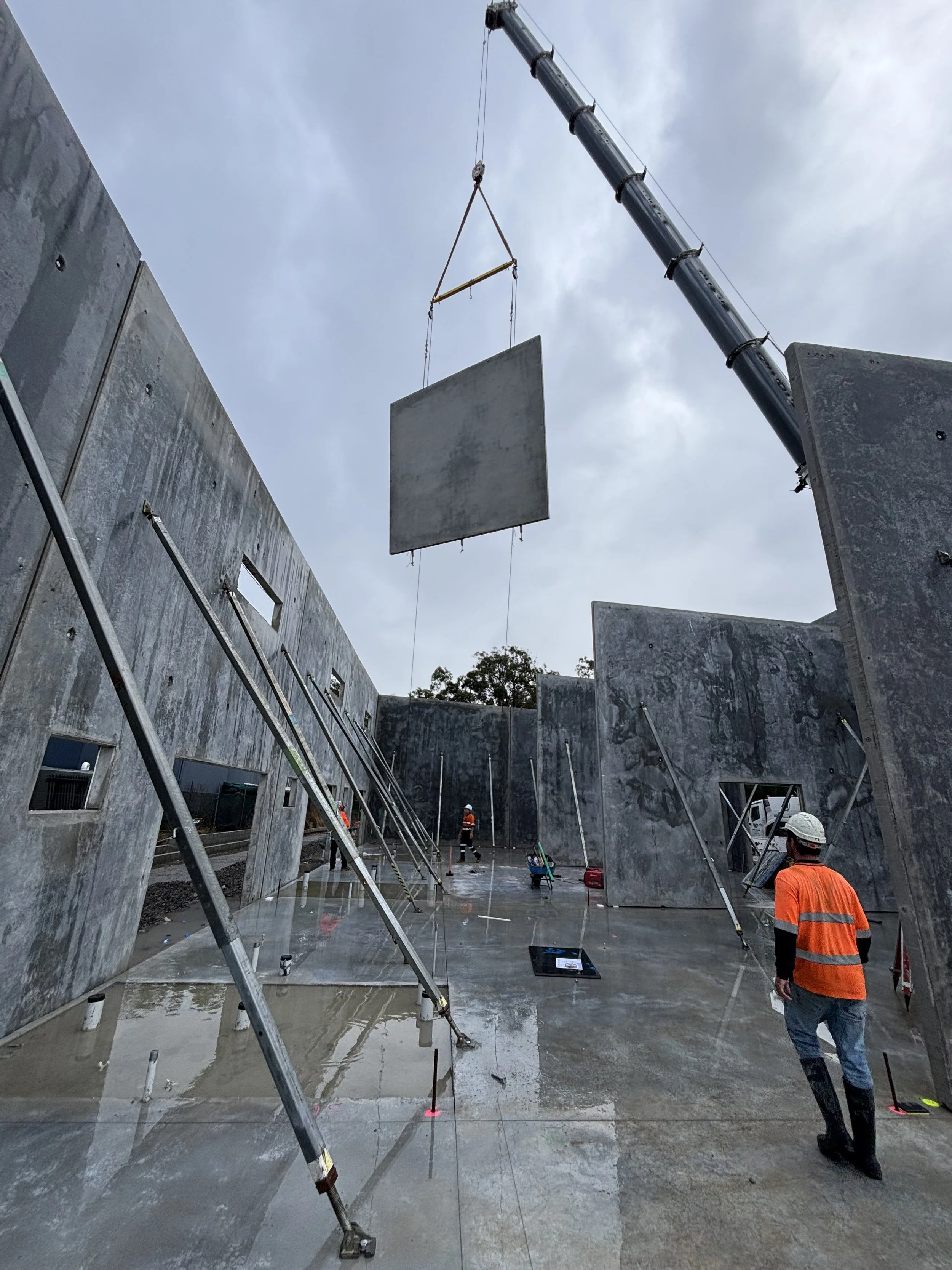 Coastal Concrete workers in safety gear working on a large commercial concrete construction site with towering walls, scaffolding, and a crane lifting a concrete tilt panel into place in Grafton.