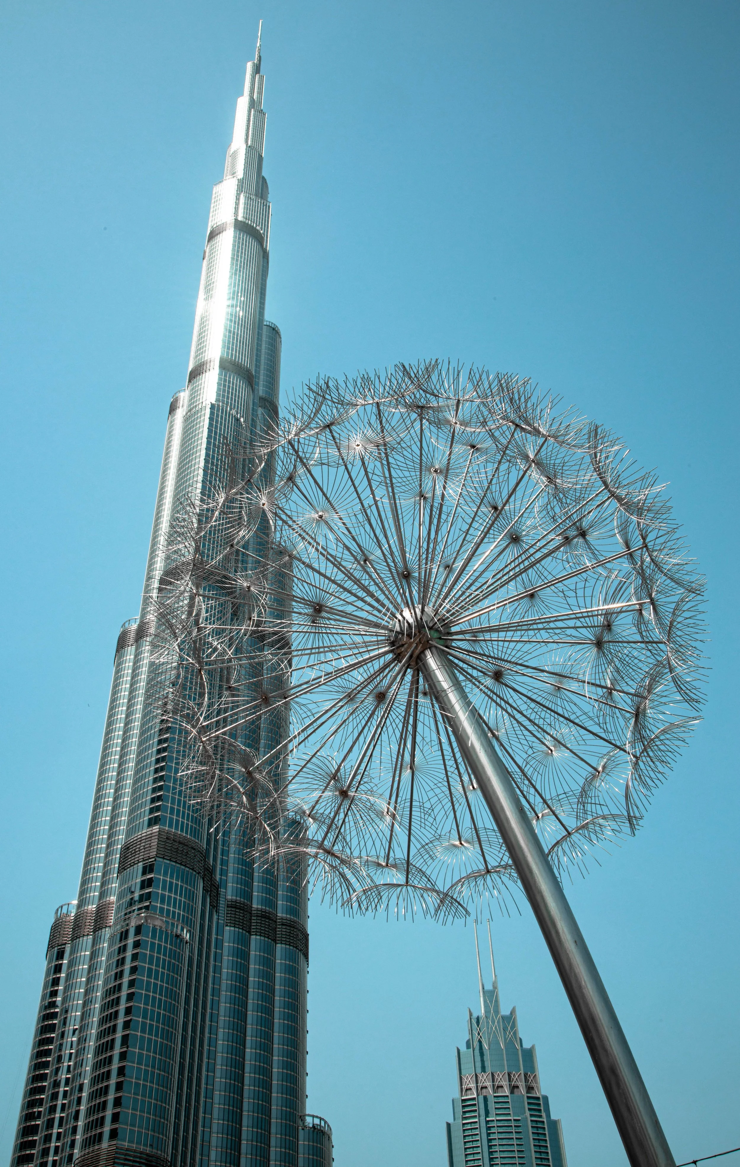 Low-angle view of the Burj Khalifa skyscraper in Dubai with a modern street lamp in the foreground against a clear blue sky.