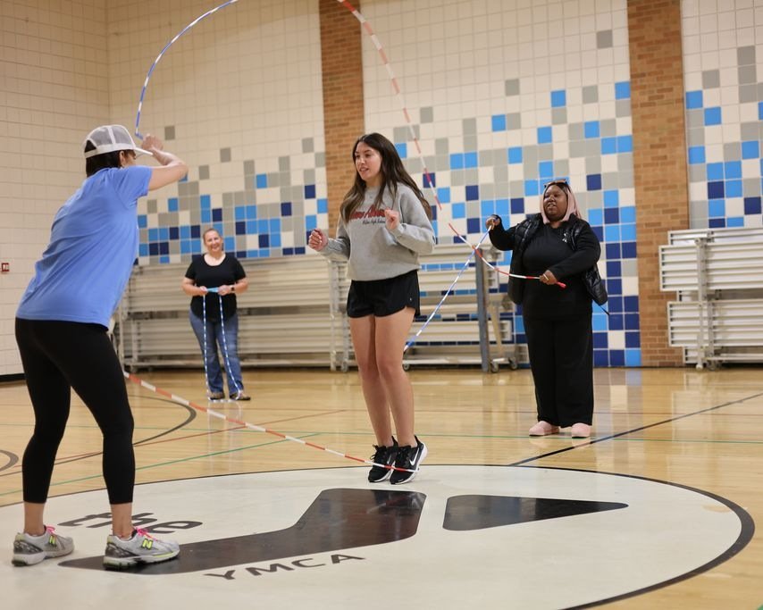 A trainee jumps double Dutch while staff turn the ropes in a YMCA gym