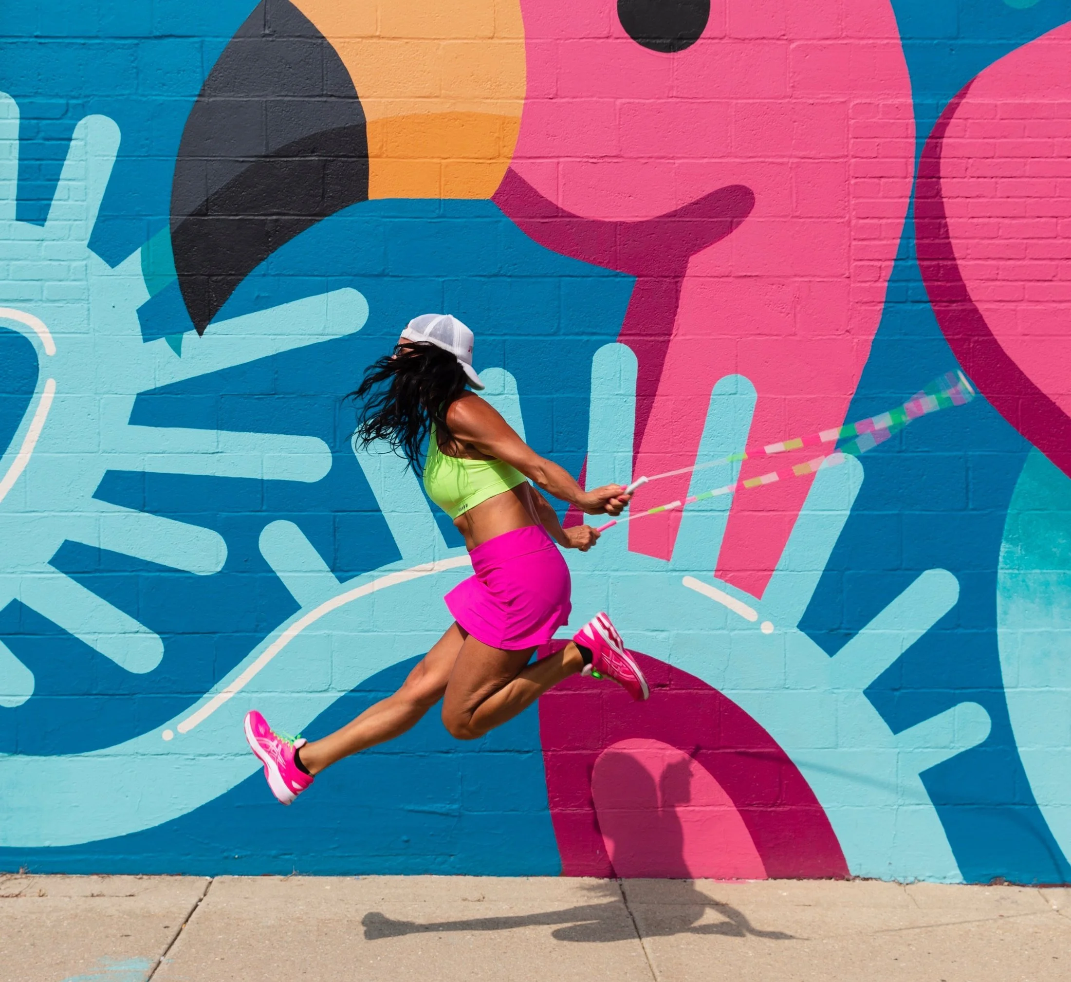Founder Cher mid-air with a jump rope in front of a colorful mural
