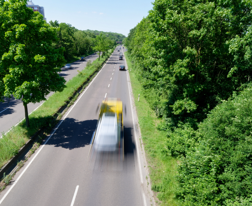 Een snelweg met voertuigen, omgeven door groene bomen en een blauwe lucht.
