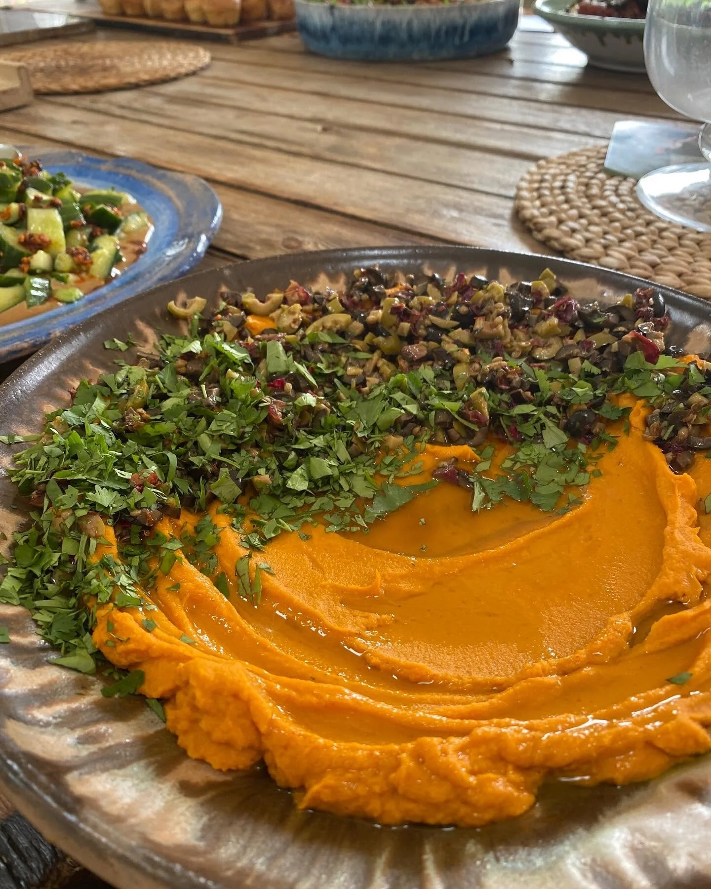A plate of bright orange mashed sweet potatoes garnished with chopped herbs, alongside a dish of chopped green vegetables and herbs, on a rustic wooden table.