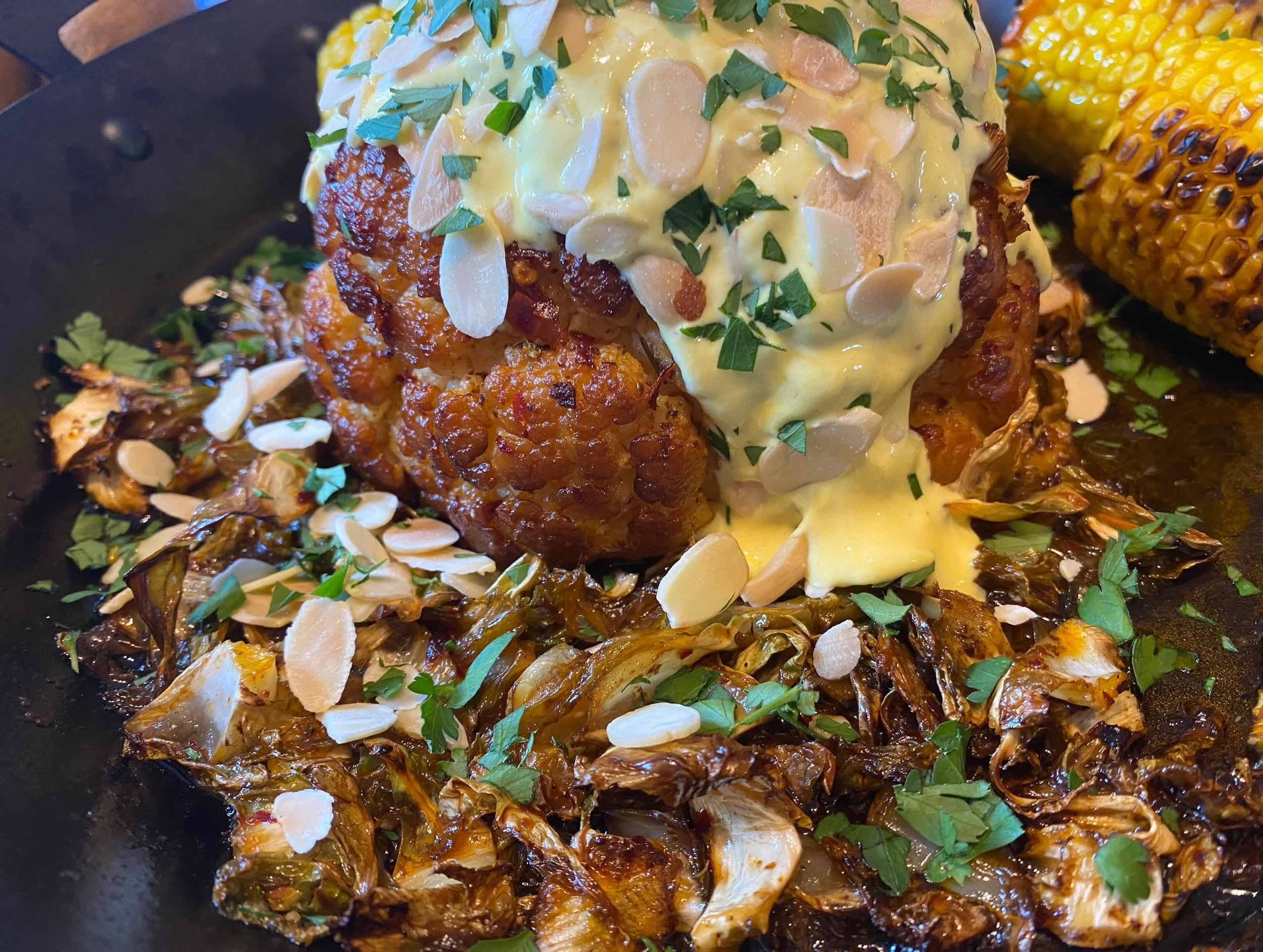 Close-up of a cooked dish with seasoned, shredded vegetables topped with almond slices and parsley, and a piece of chicken covered with a yellow sauce.