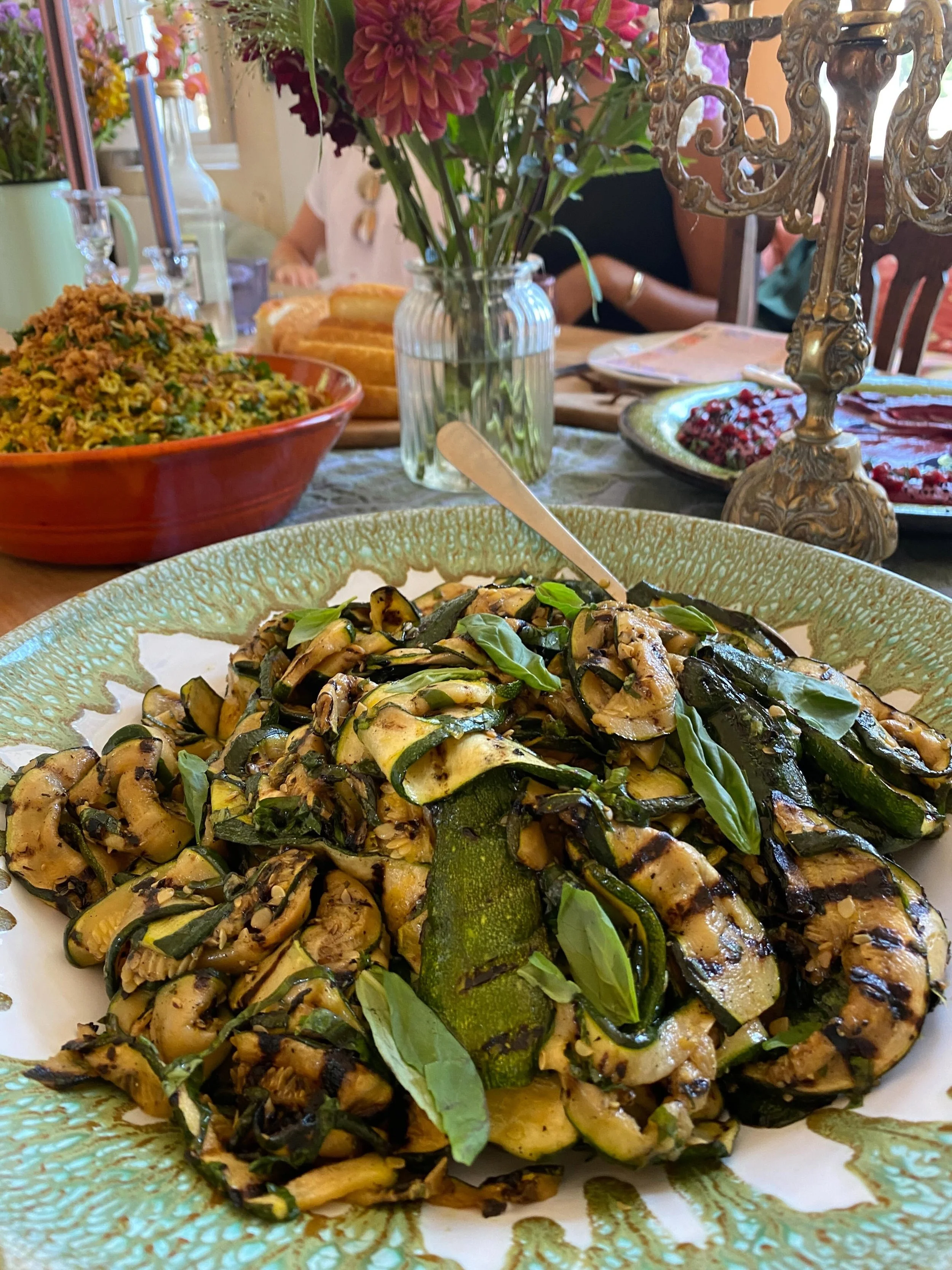 Close-up of grilled zucchini slices garnished with fresh basil on a decorative plate at a dining table.