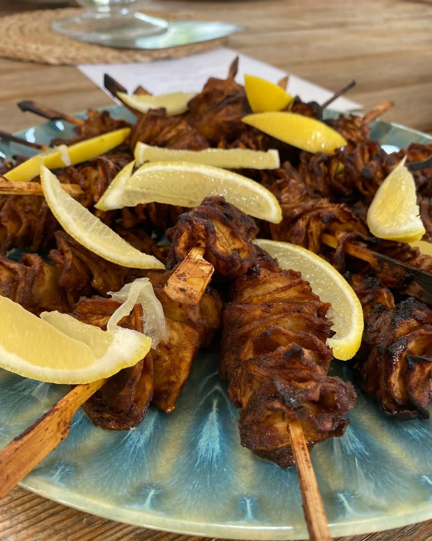 Close-up of grilled meat skewers on a decorative blue plate garnished with lemon wedges.