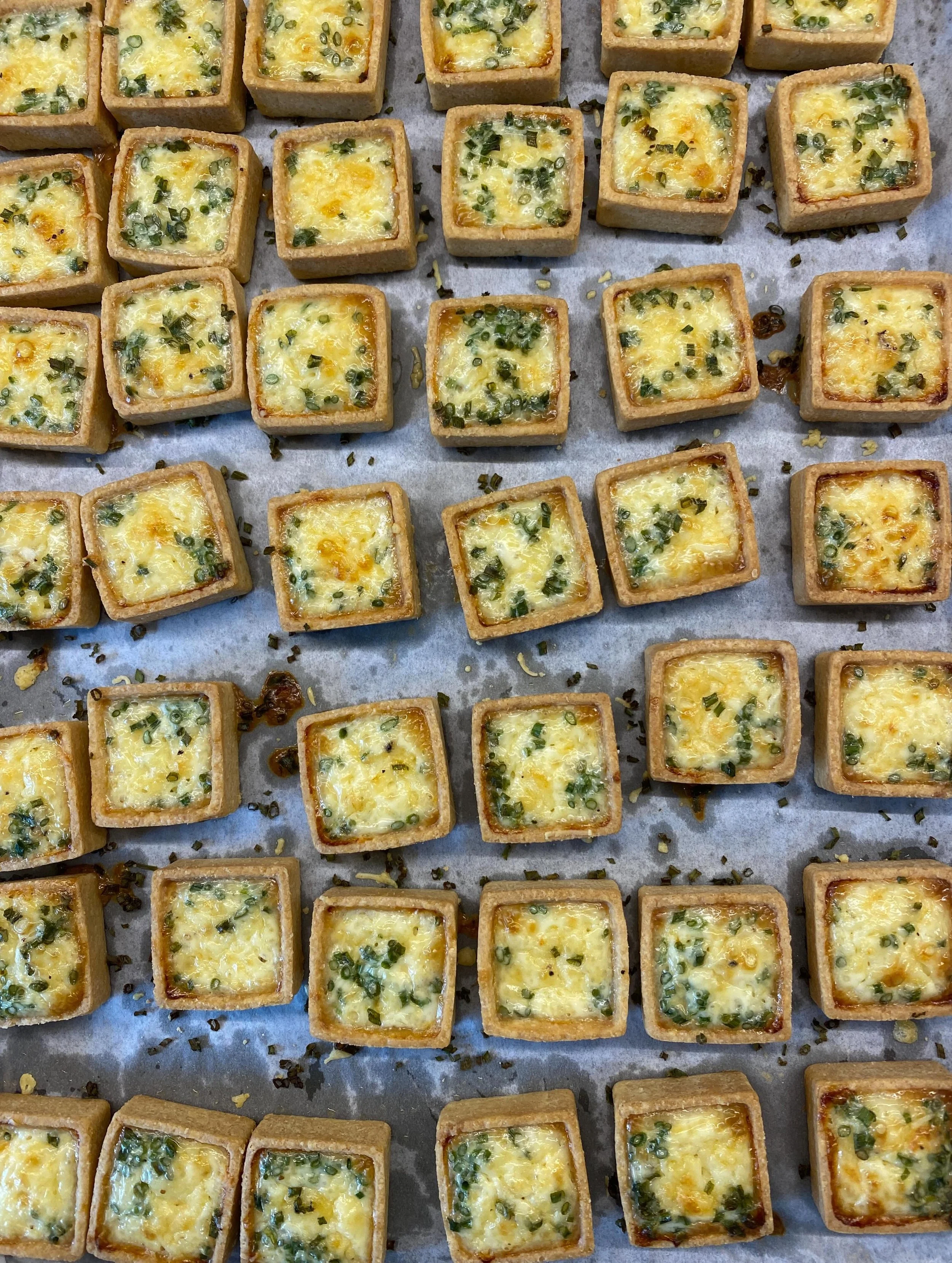 Bite-sized square cheese toasts garnished with chopped green onions on a baking sheet.
