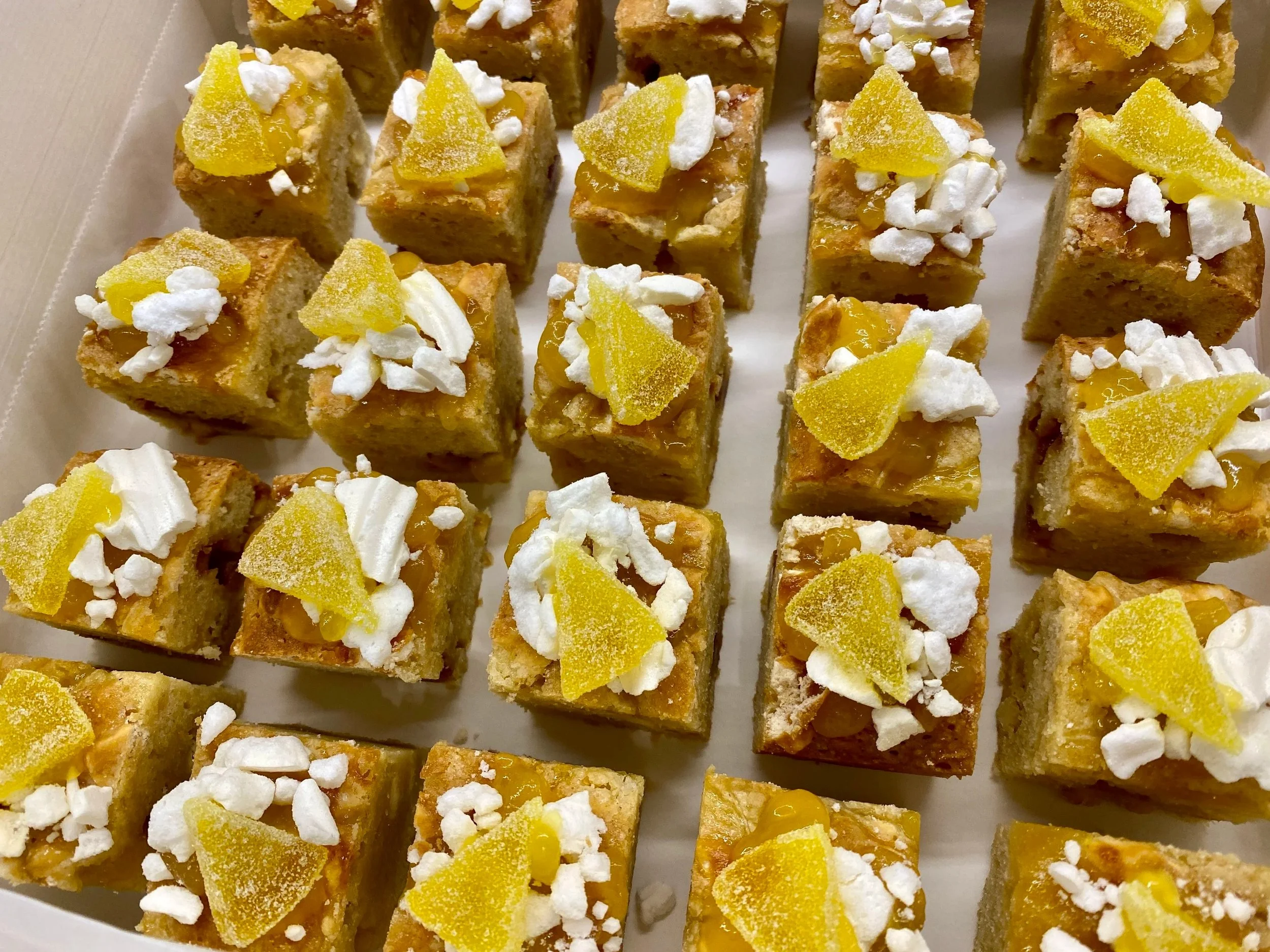 A tray of small lemon bars topped with white icing and yellow lemon candy pieces.