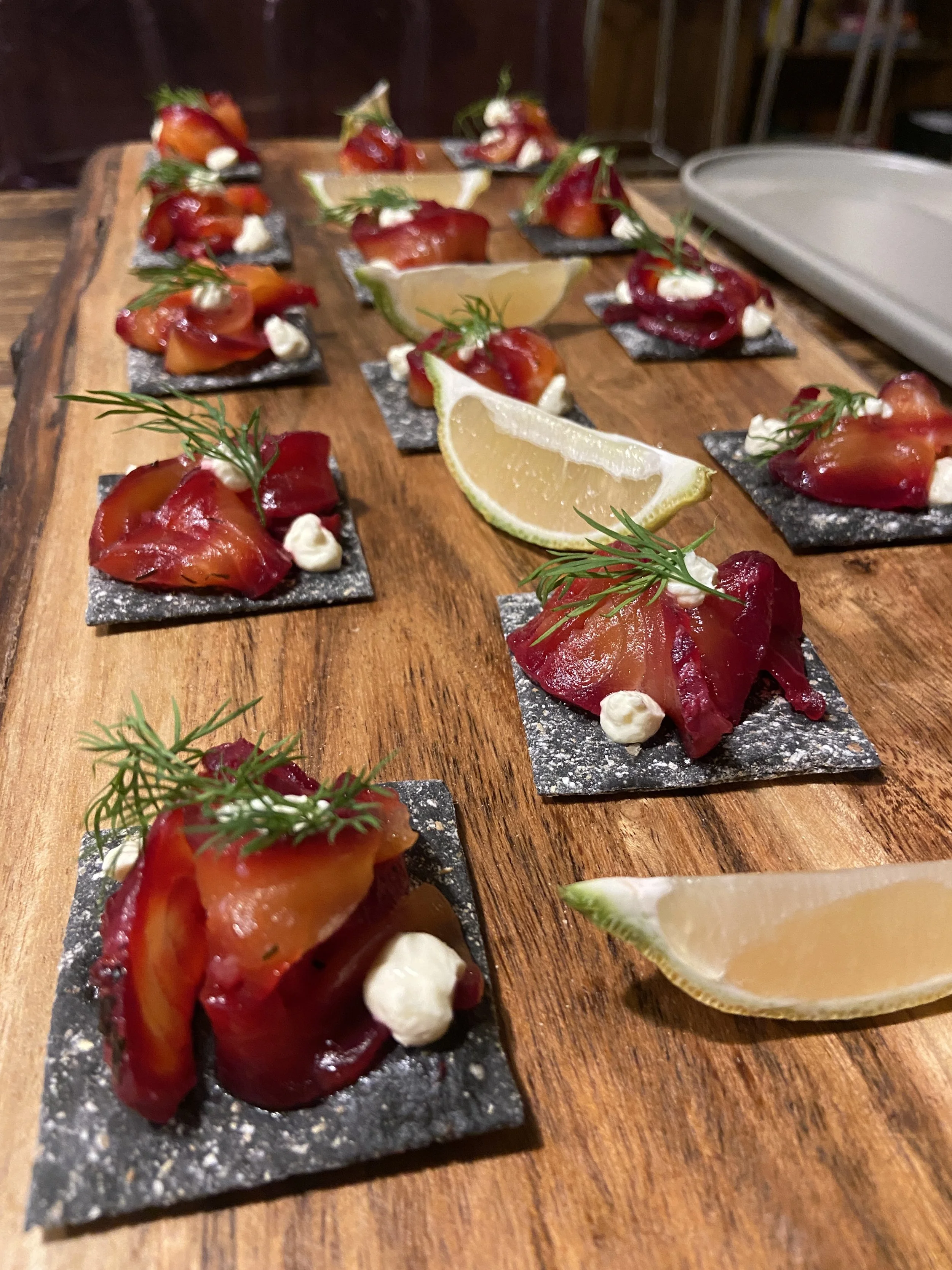 Small appetizer plates with smoked salmon, lemon wedges, garnished with herbs, served on black slate bases on a wooden surface.