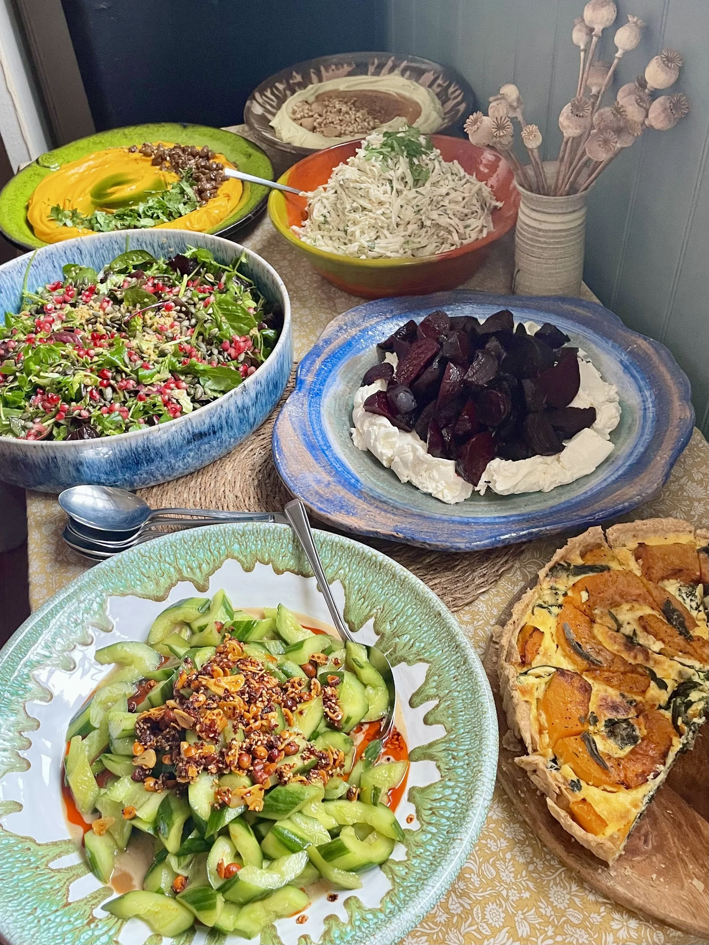 A table with an assortment of salads, a vegetable tart, and a panna cotta dessert with chocolate and toppings.
