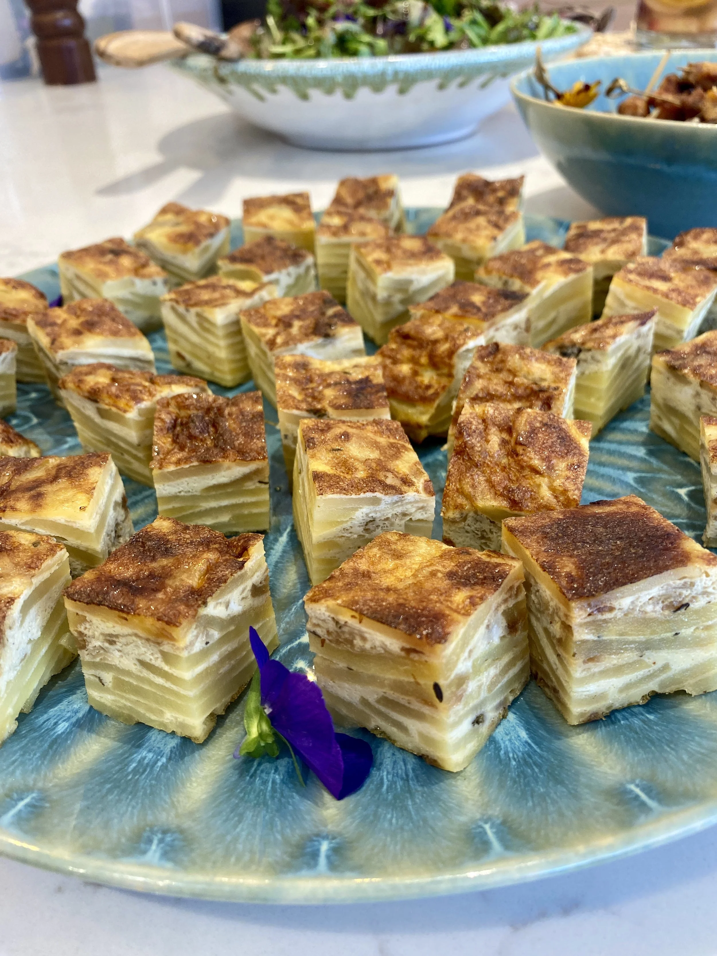 A plate of layered potato gratin with a golden-brown crust, garnished with purple flowers.