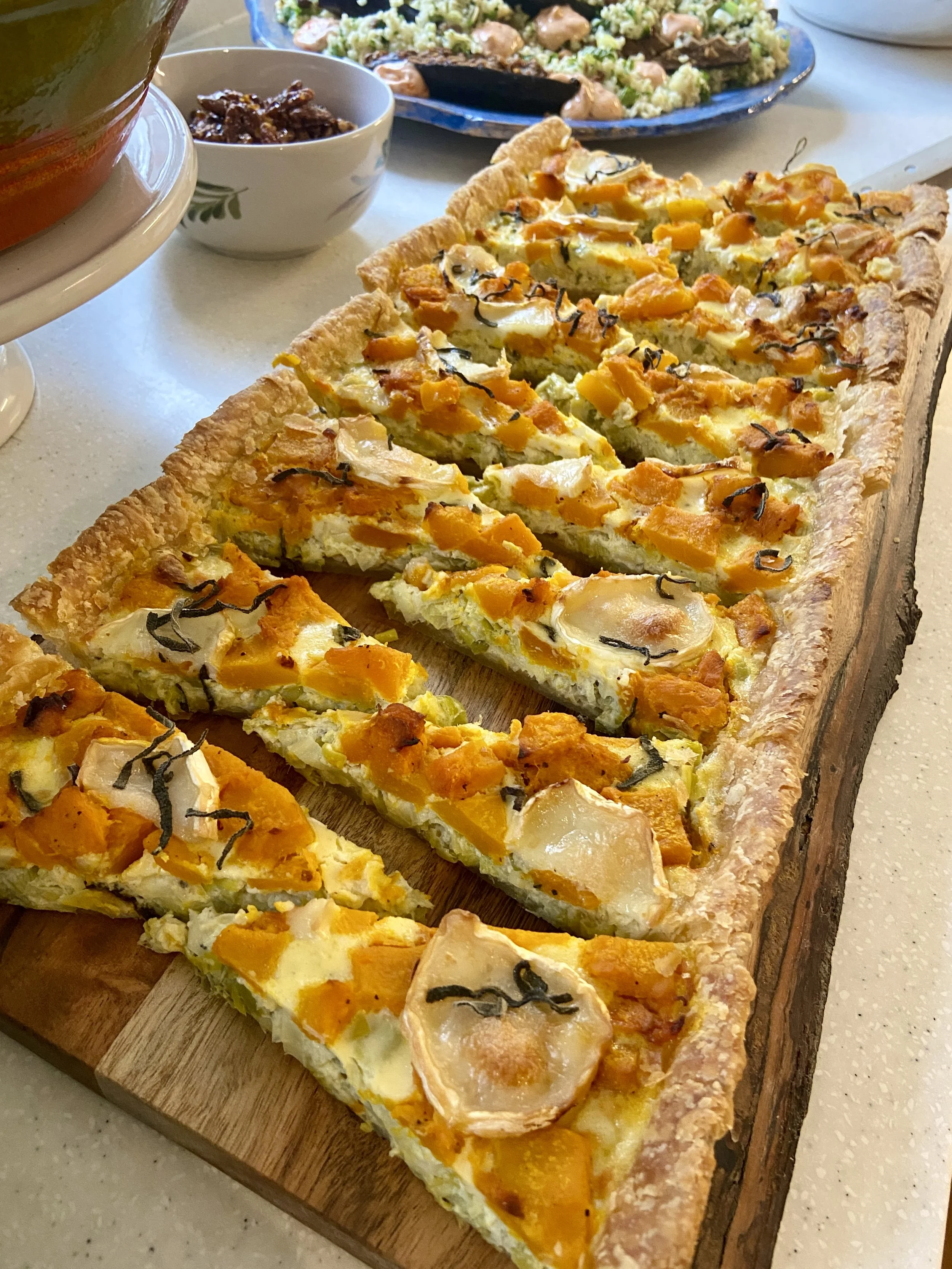 A sliced vegetable quiche on a wooden serving board, with a golden crust and colorful fillings of squash, carrots, and possibly zucchini.
