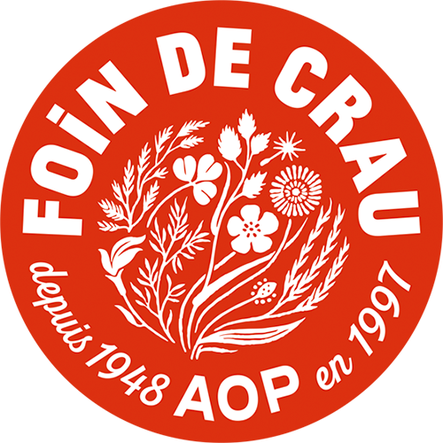 Logo circulaire rouge avec des fleurs blanches et des feuilles, texte en blanc « Foin de Crau » en haut, « AOP en 1997 » en bas, et « depuis 1948 » sur le côté