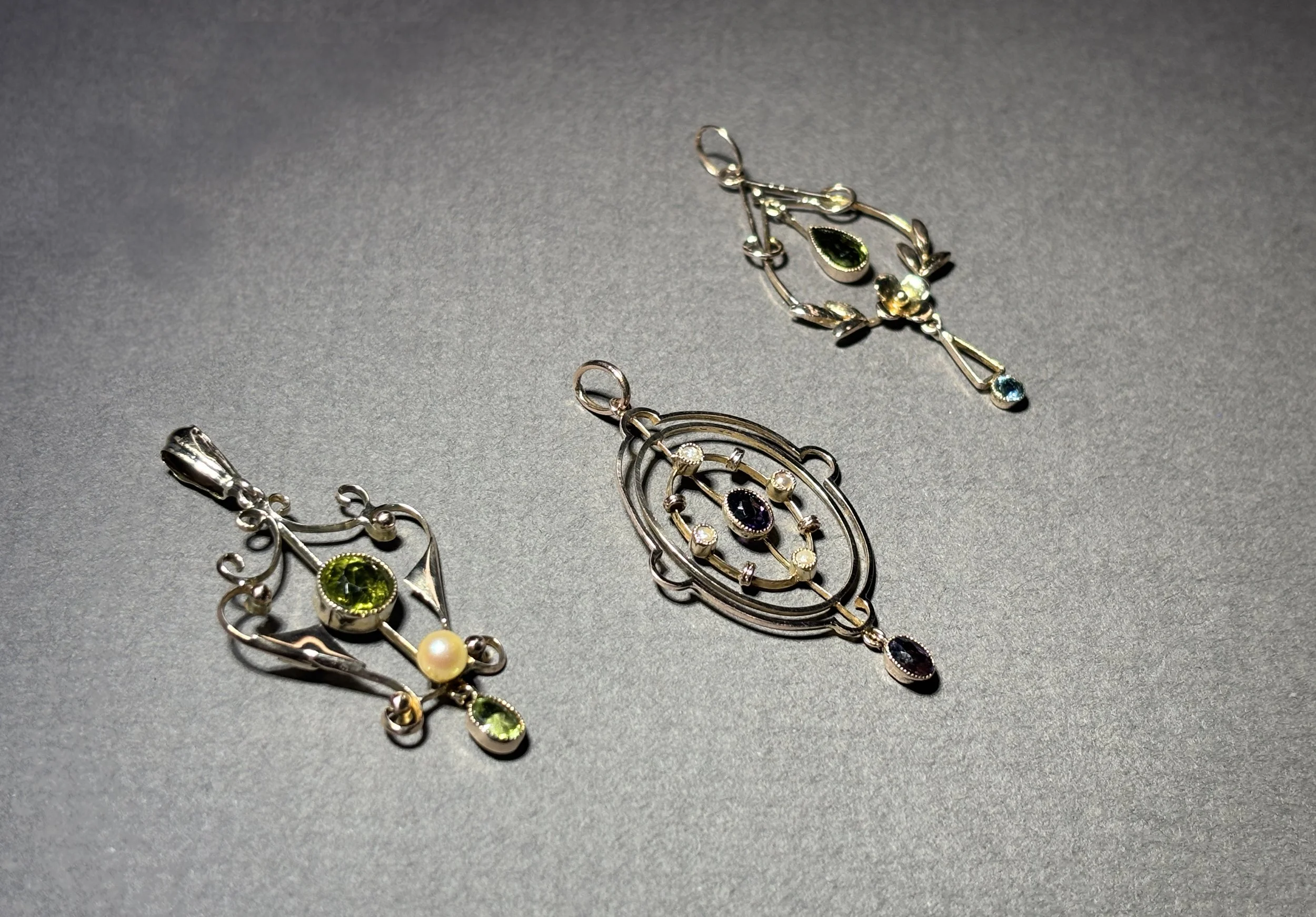 Three silver jewelry pendants with colorful gemstones on a gray background.