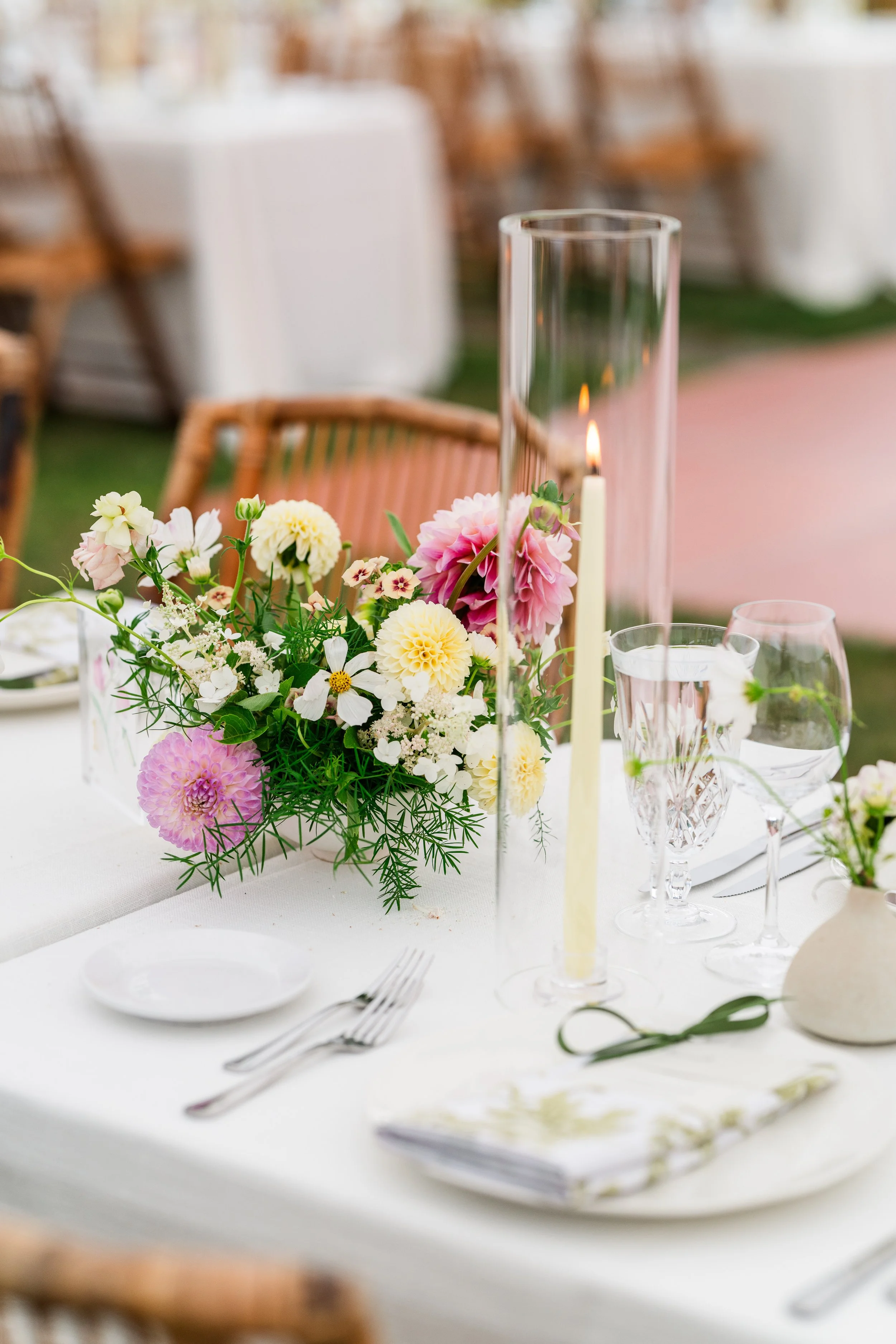 Elegant table setting with a floral centerpiece and tall candle holder, set for a special event or wedding, with tableware and glasses on a white tablecloth.
