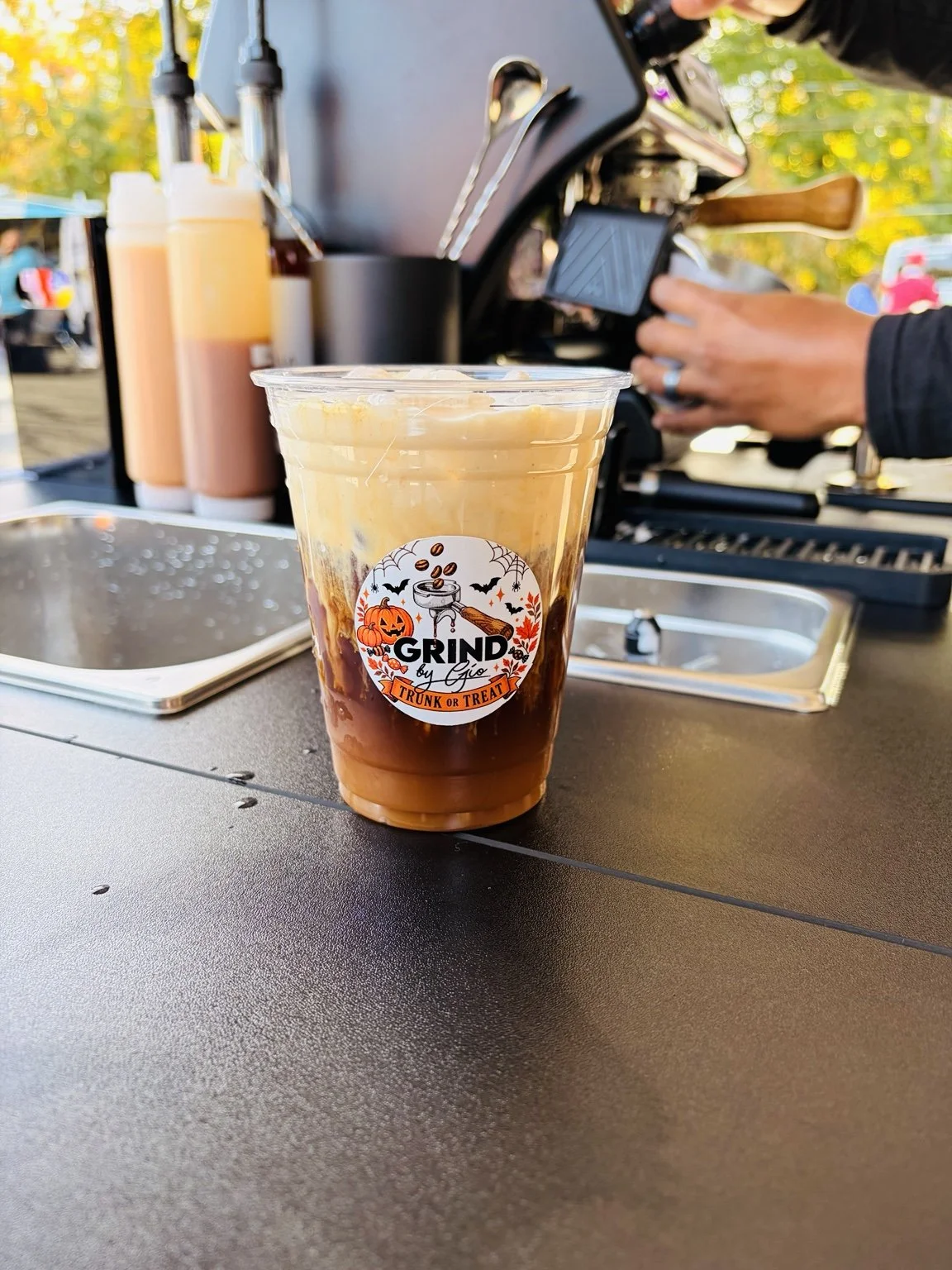 Iced coffee with the Grind by Gio logo beside the espresso machine
