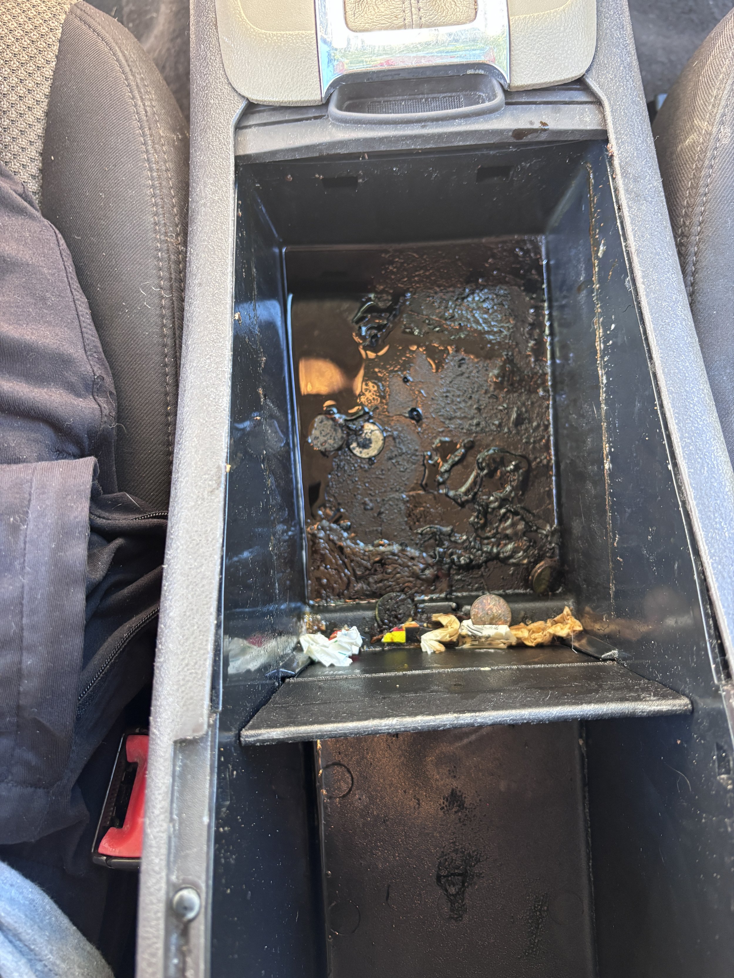 Car center console filled with dirty melted ice, trash, and coins.