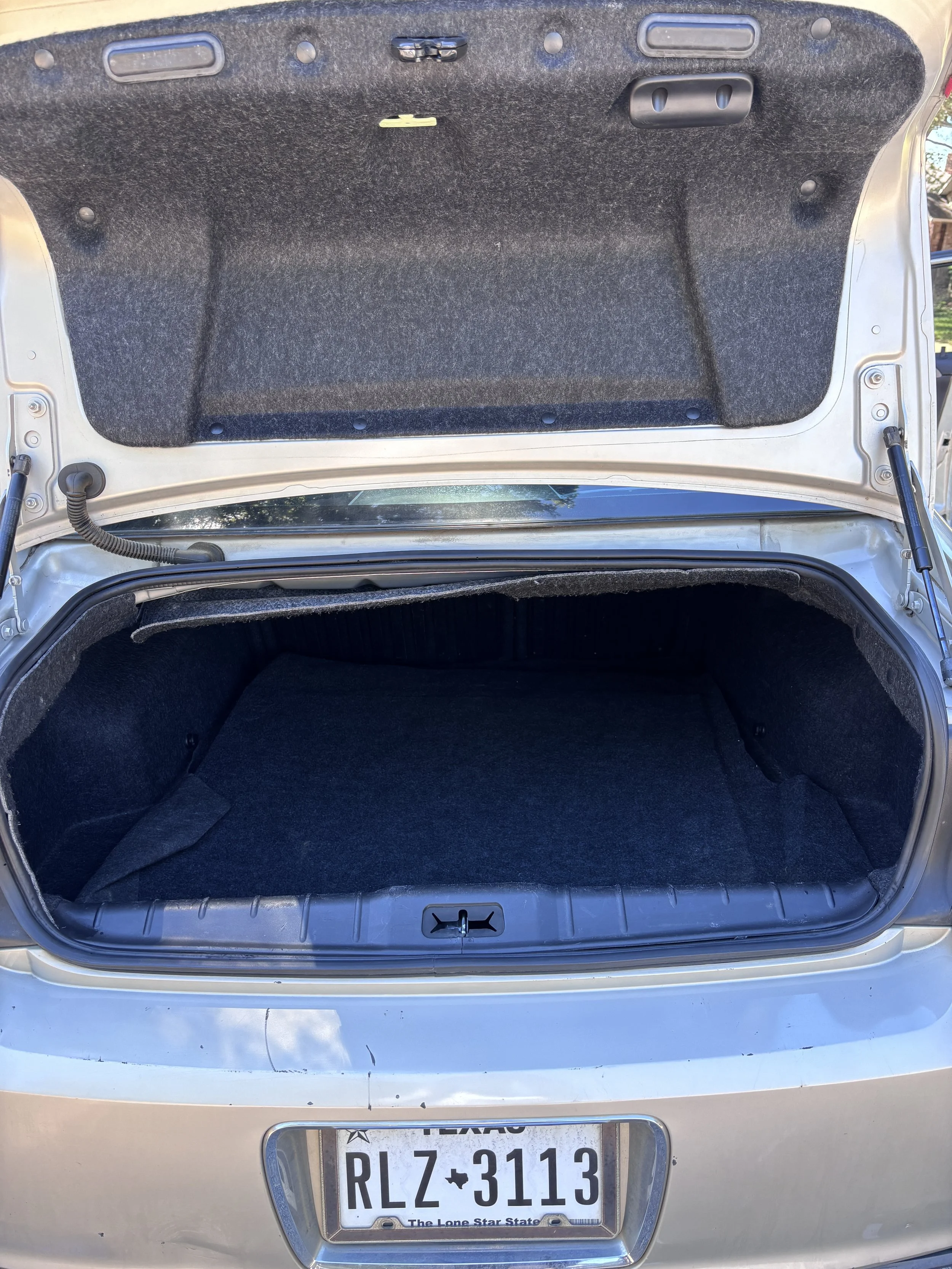 The open trunk of a silver car showing the black interior with a Texas license plate that reads RLZ-3113.