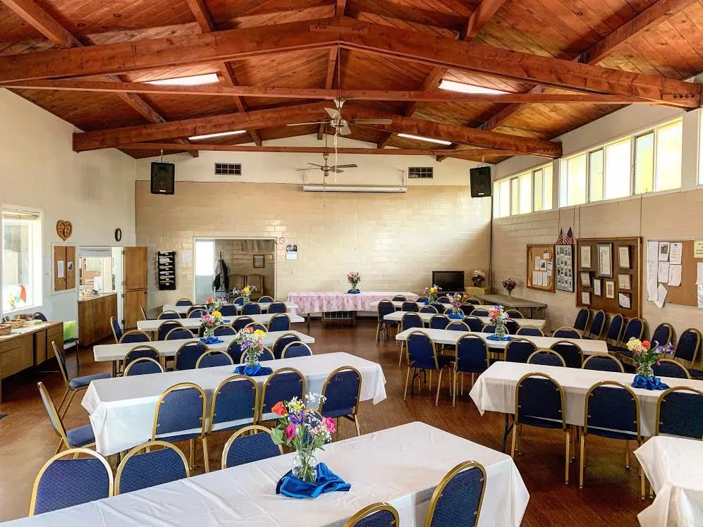 A decorated event hall with long tables covered in white tablecloths and small floral centerpieces, set up for a gathering or celebration.