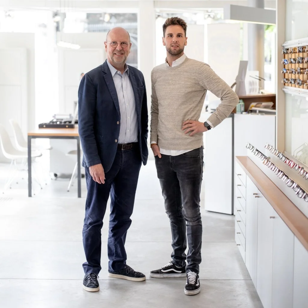 Two men standing in a bright eyewear showroom beside displays of eyeglass frames.
