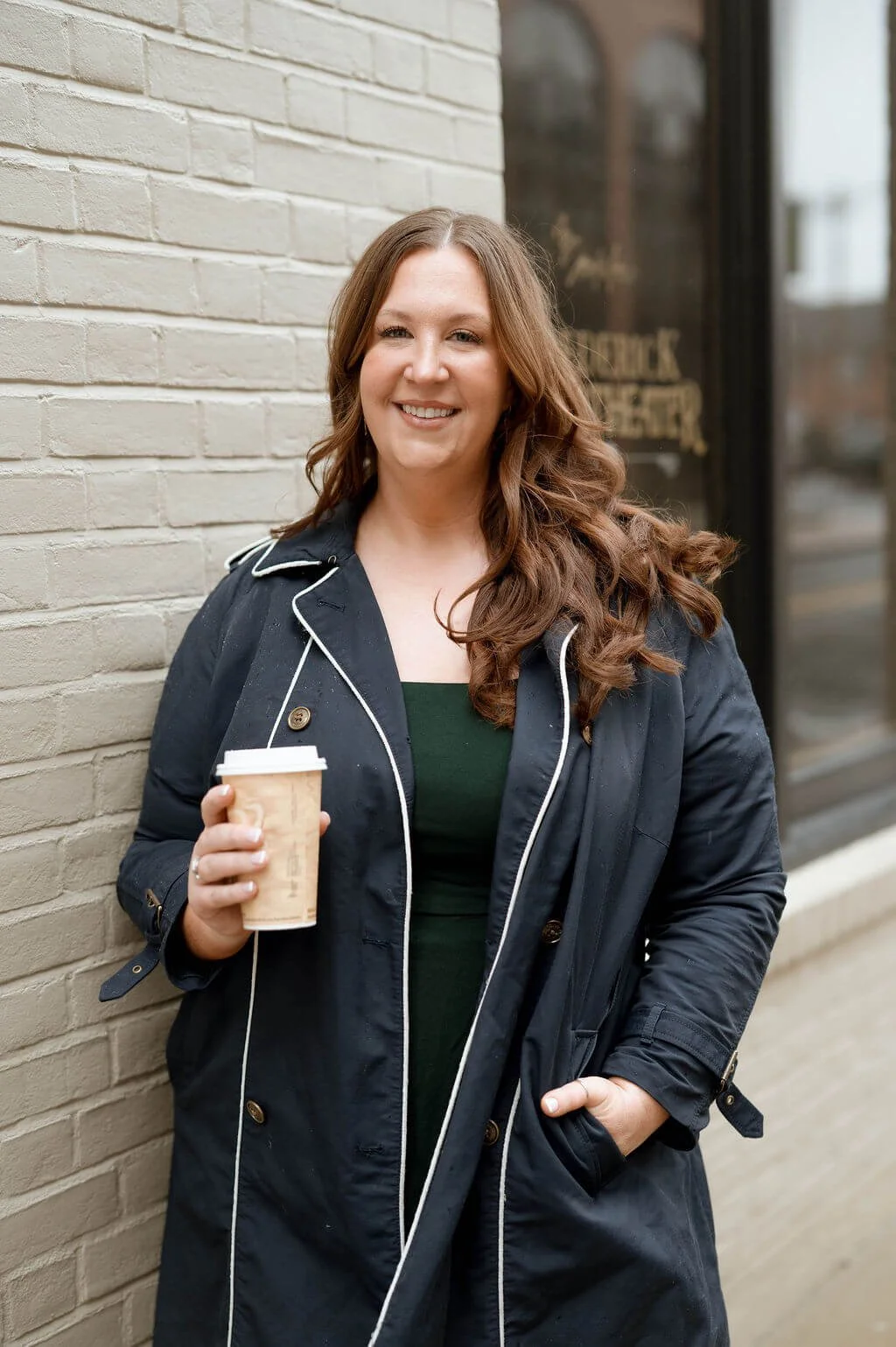 Mary Neubauer, REALTOR®, holding a coffee in front of a brick wall