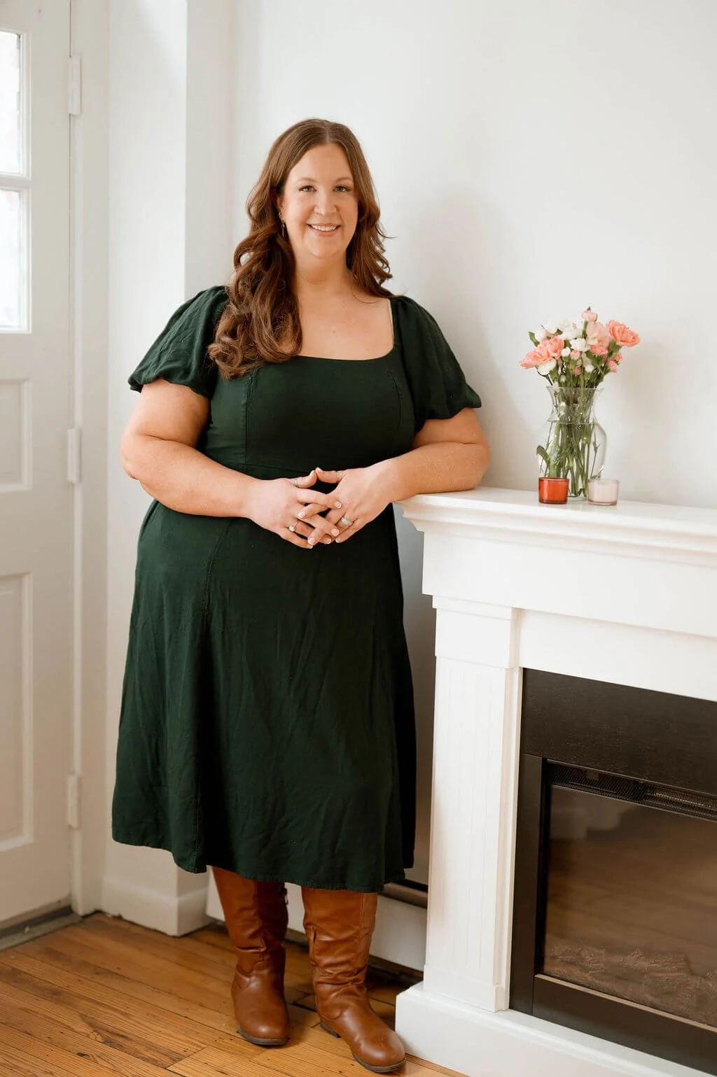 Mary Neubauer, REALTOR®, standing beside a fireplace with a vase of flowers