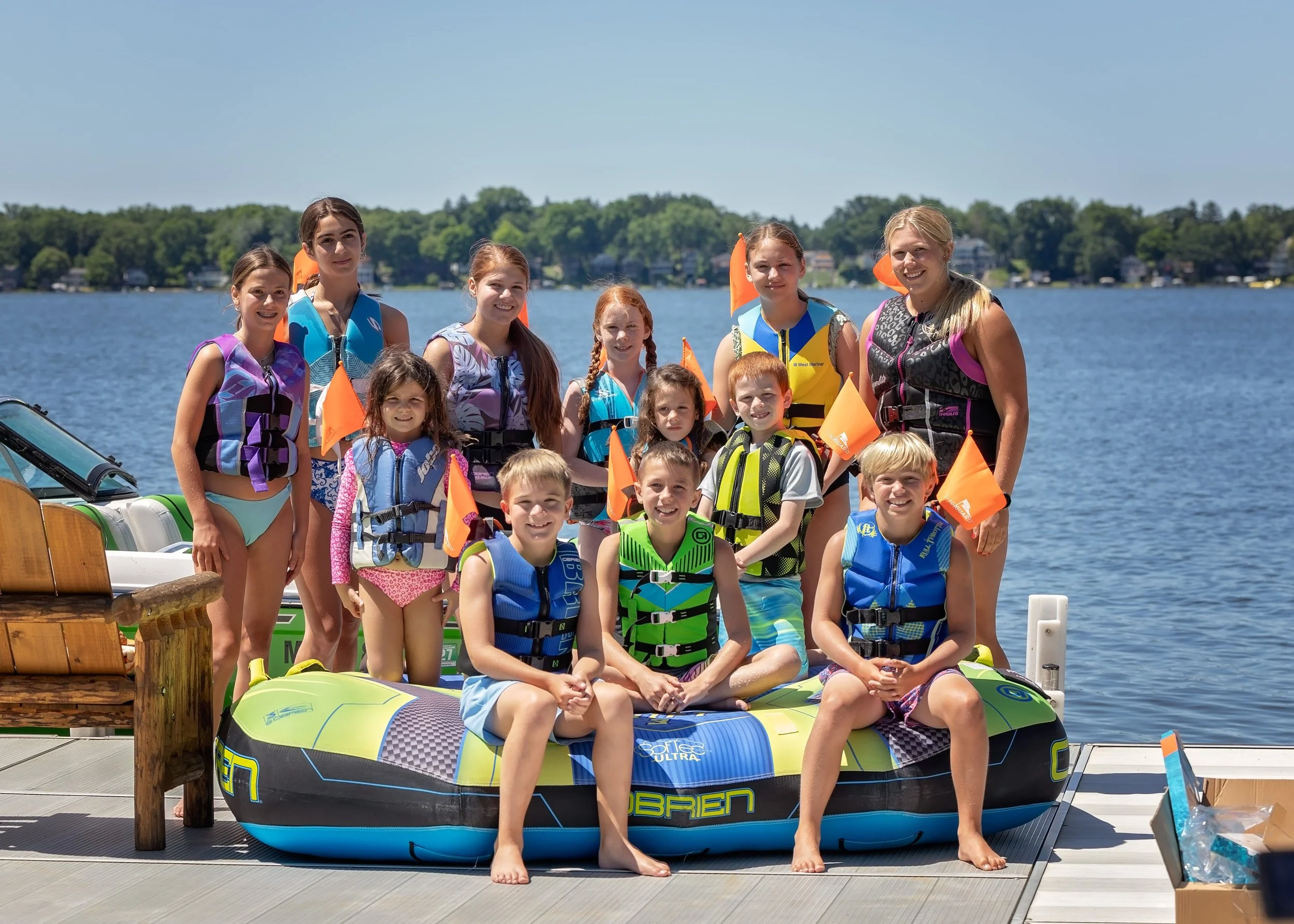 A group of children and a woman on a dock by the water, wearing paddleboards and life jackets and using the patented FlagGuard system to increase visibility, smiling at the camera on a sunny day.