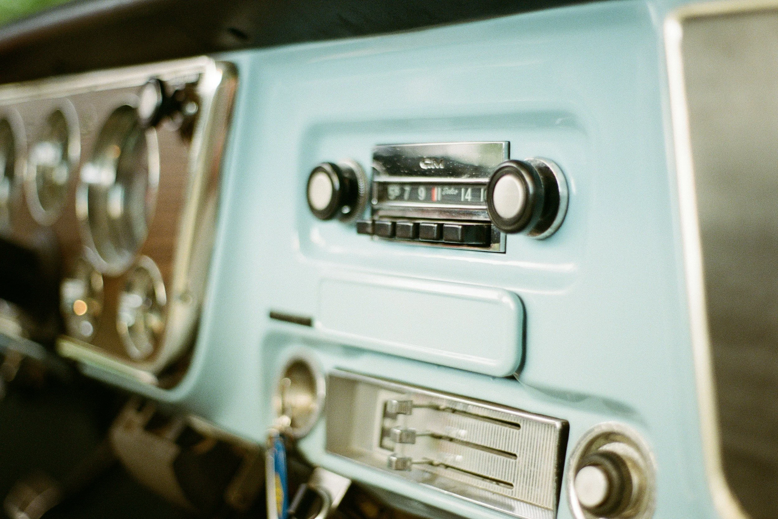 Close-up of a vintage car radio with black dials and buttons, set in a light-colored dashboard.