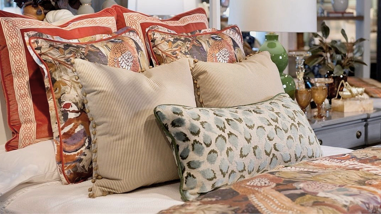 A neatly made bed with multiple decorative pillows of various colors and patterns, including floral, striped, and animal print, in a cozy, well-decorated bedroom.