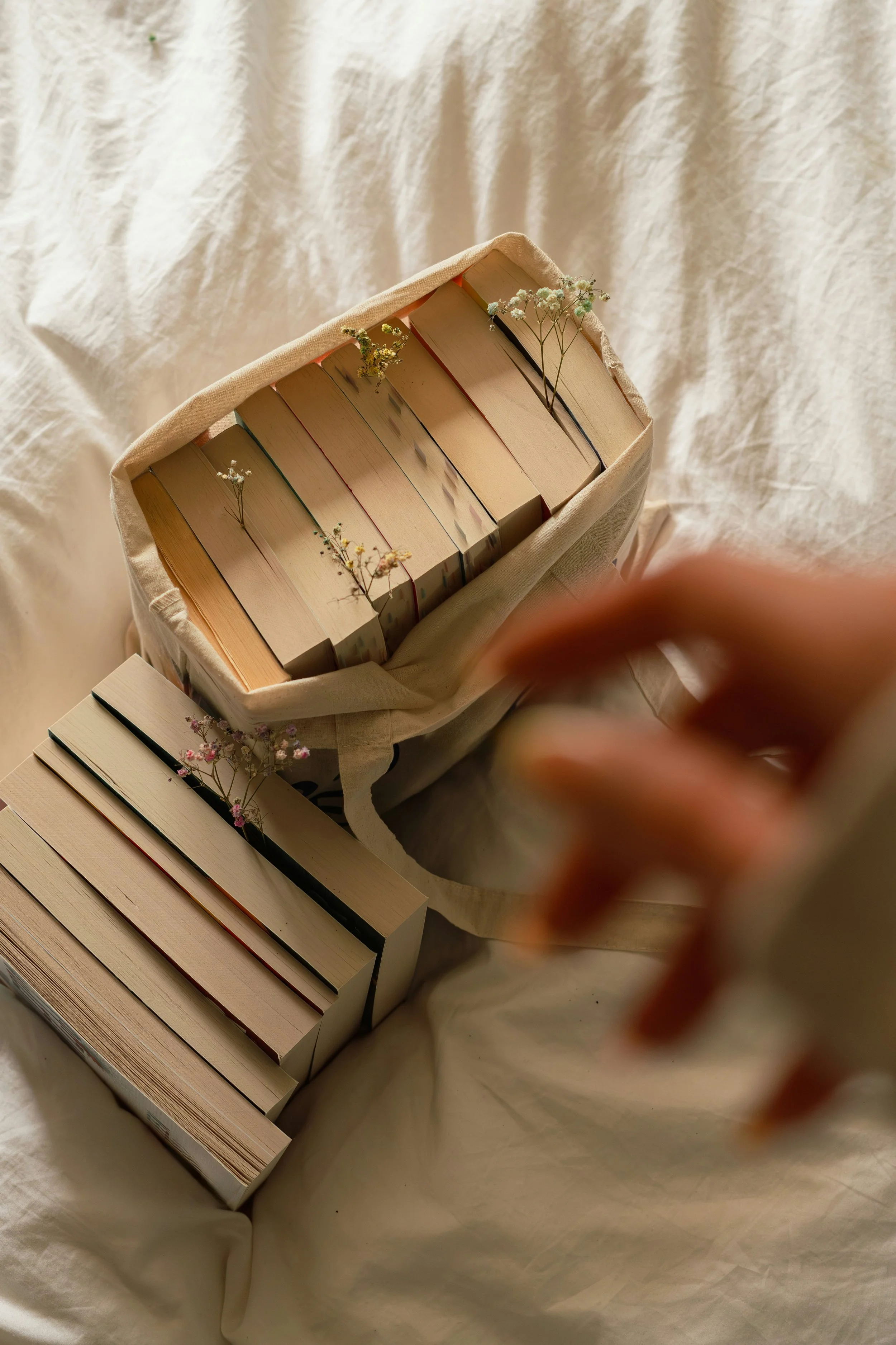Open books in a fabric bag with small white and pink flowers, set against a beige cloth background.
