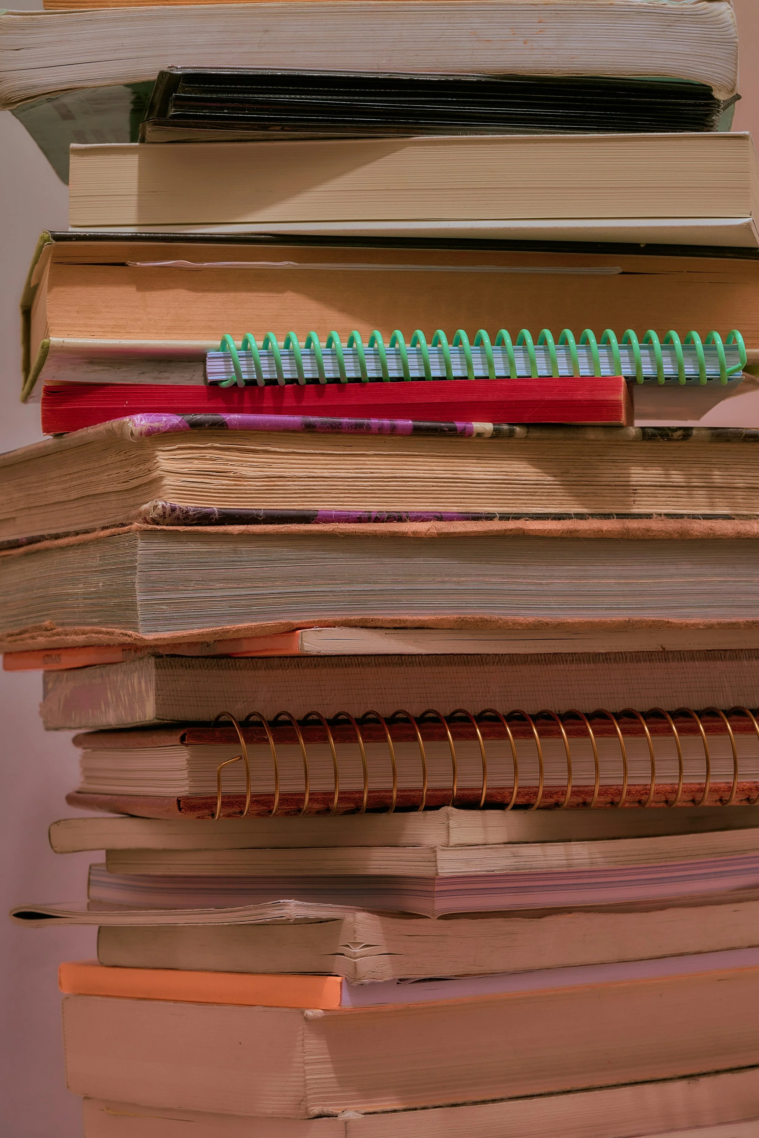 A stack of various books and notebooks seen from the side, with some pages and covers visible. The books vary in size, color, and condition.