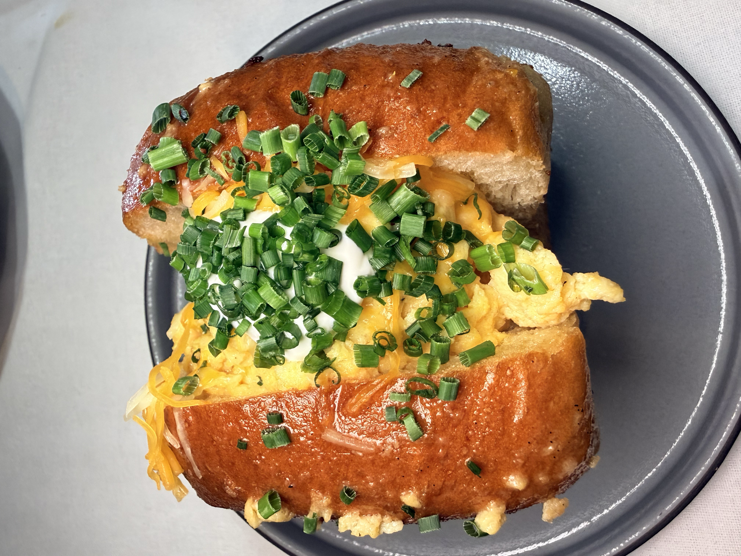 A plate of baked french bread topped with scrambled eggs, shredded cheddar cheese, chopped green onions, and herbs.