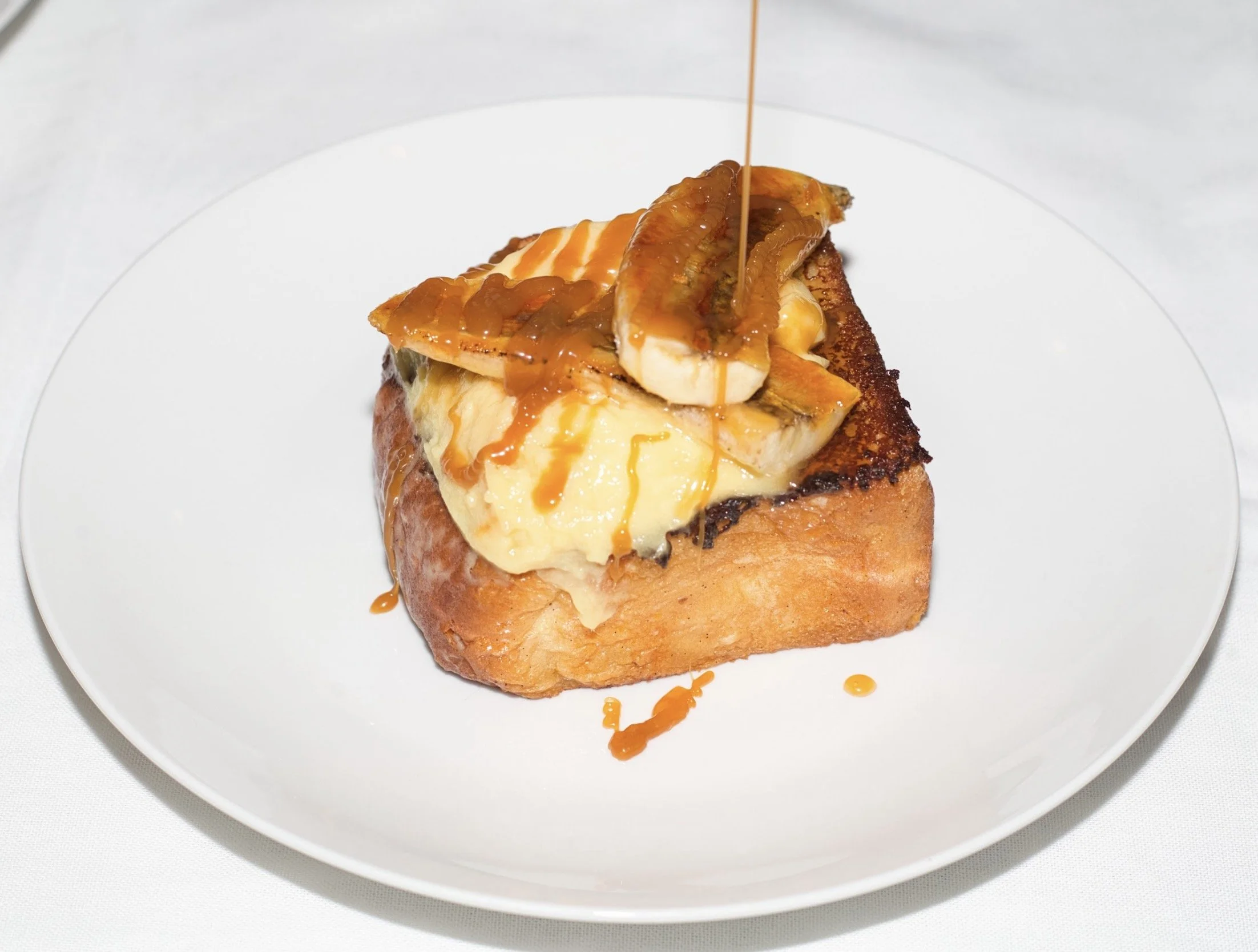 A slice of bread topped with cheese, caramelized bananas, and a drizzle of caramel sauce on a white plate.