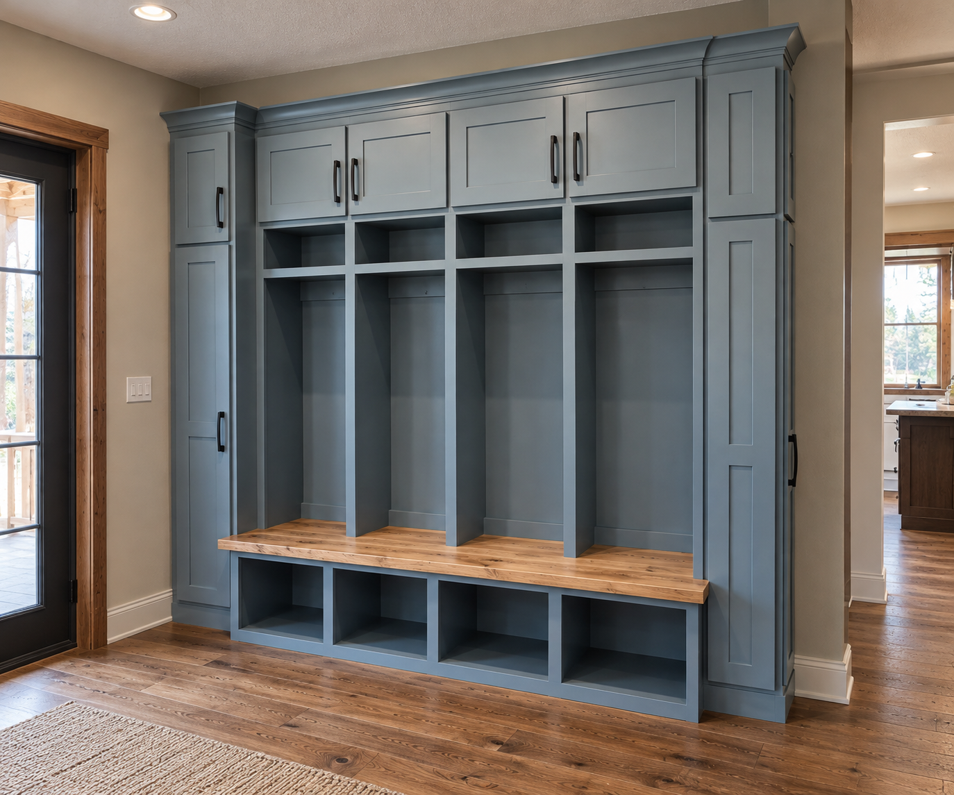 Blue built-in mudroom storage with cubbies, upper cabinets, and a wooden bench, situated near a door with a window.