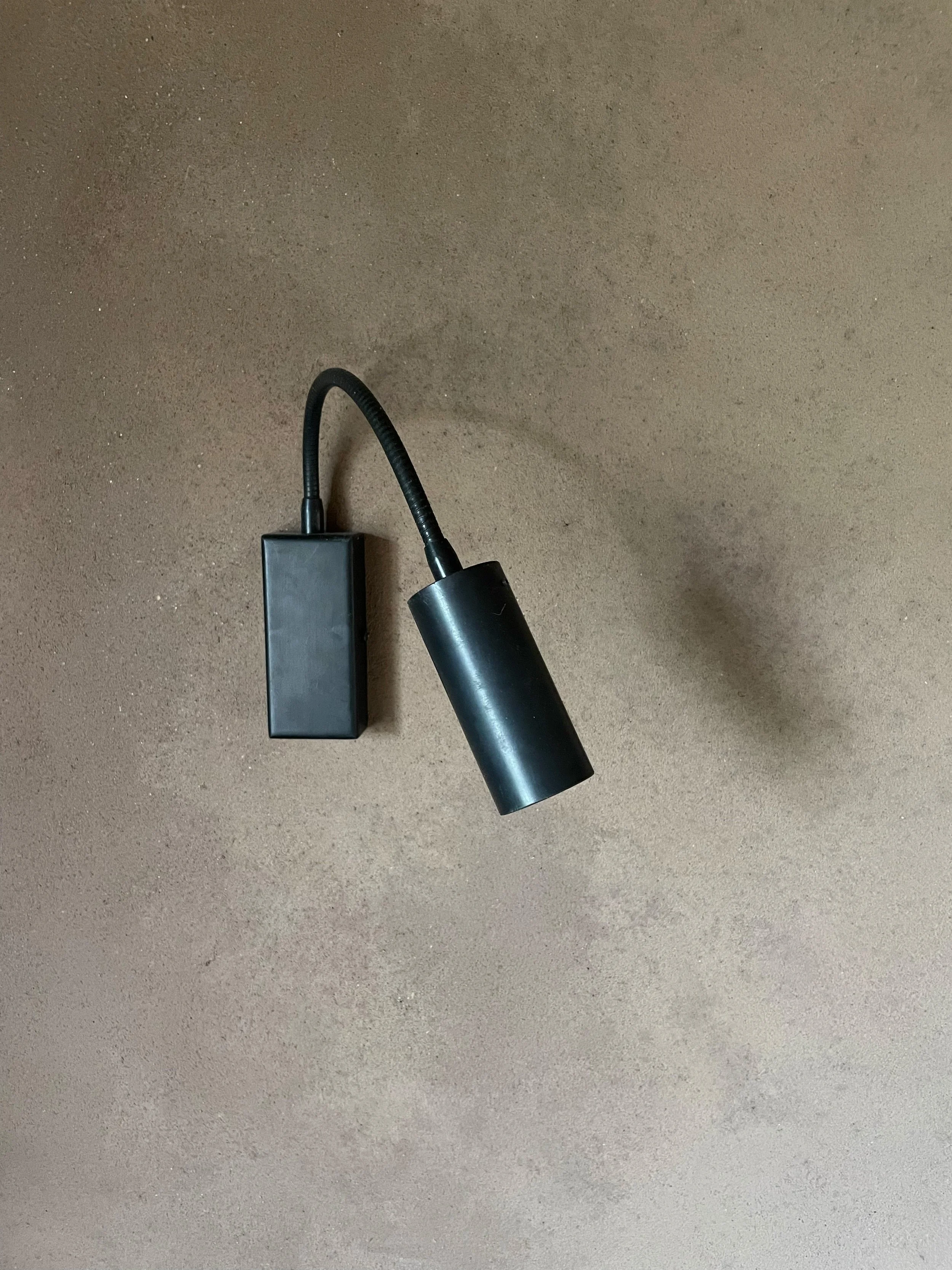 A black electrical device with a curved cord, lying on a brown surface.