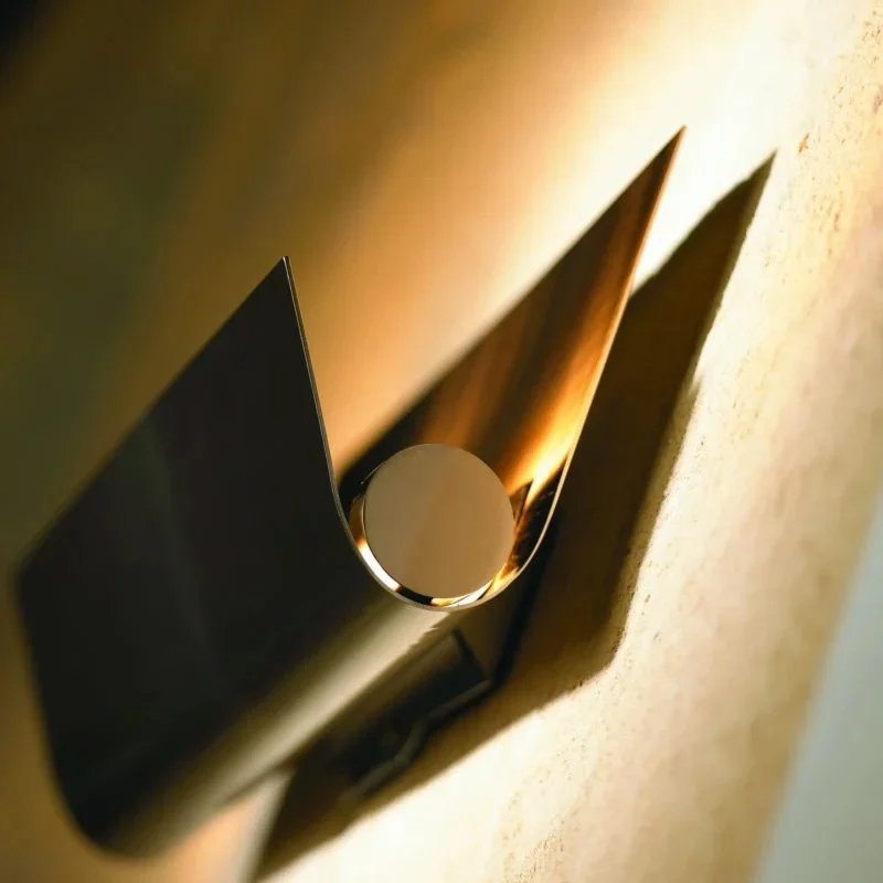 Close-up of a metallic, sculptural wall art piece with a circular element casting a shadow on a textured wall.