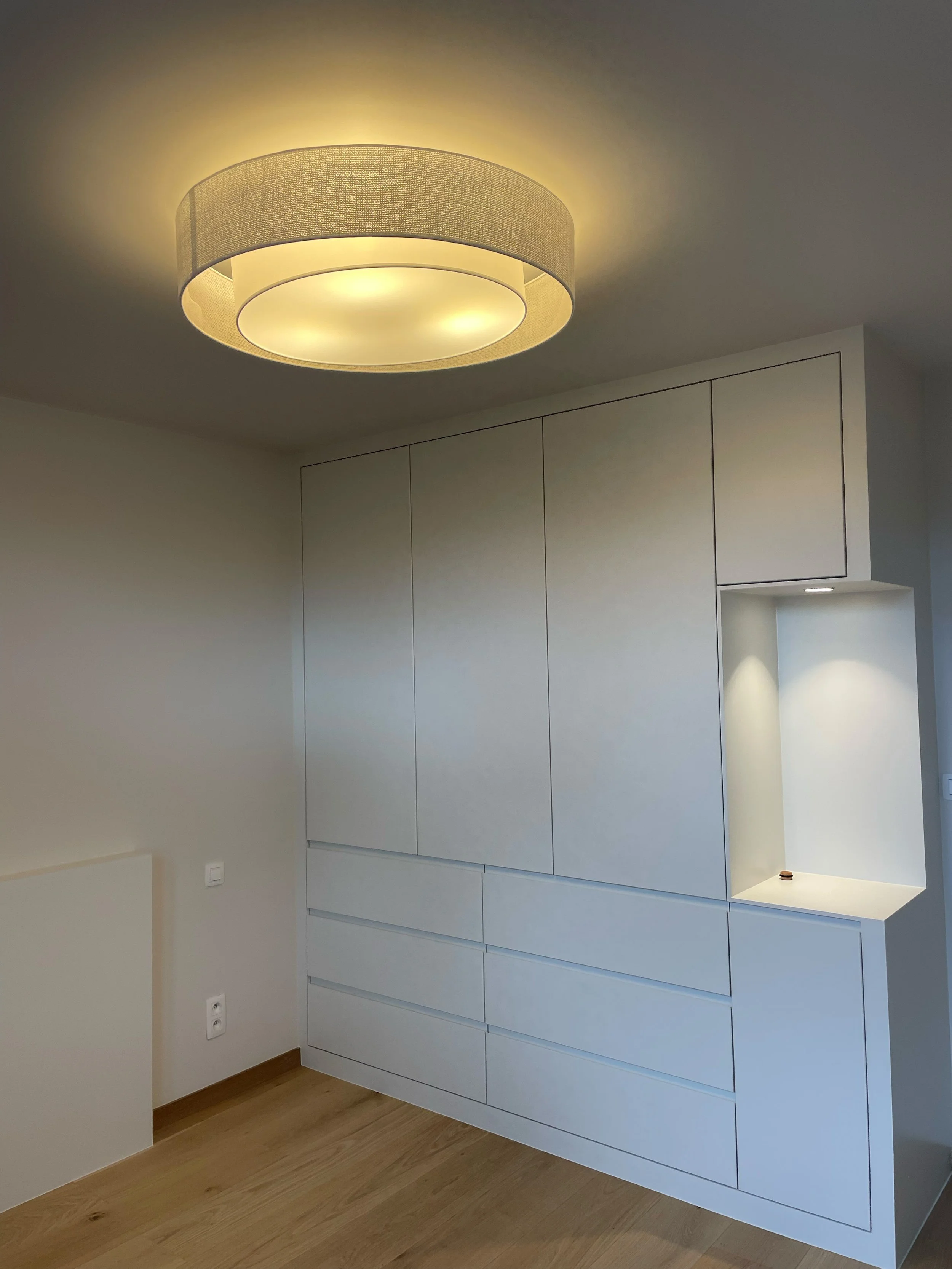 Modern white cabinet against light-colored wall with wooden floor and ceiling light fixture.