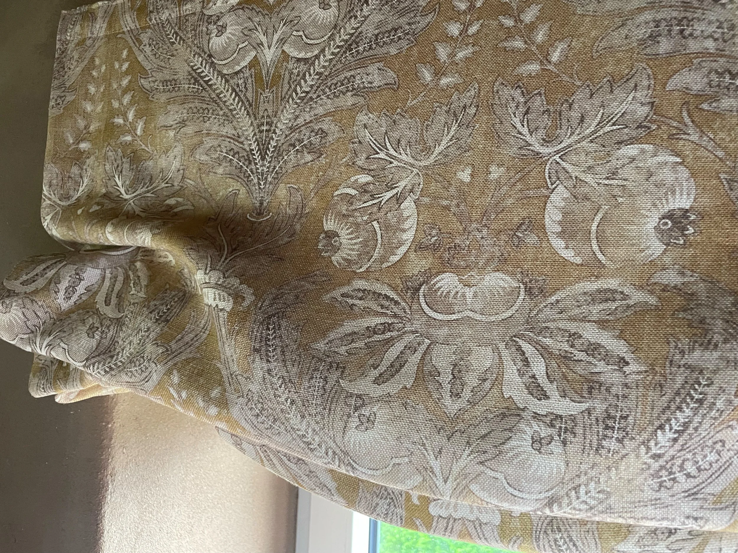 Close-up of beige fabric with intricate white floral and leaf patterns, possibly part of upholstery or drapery.