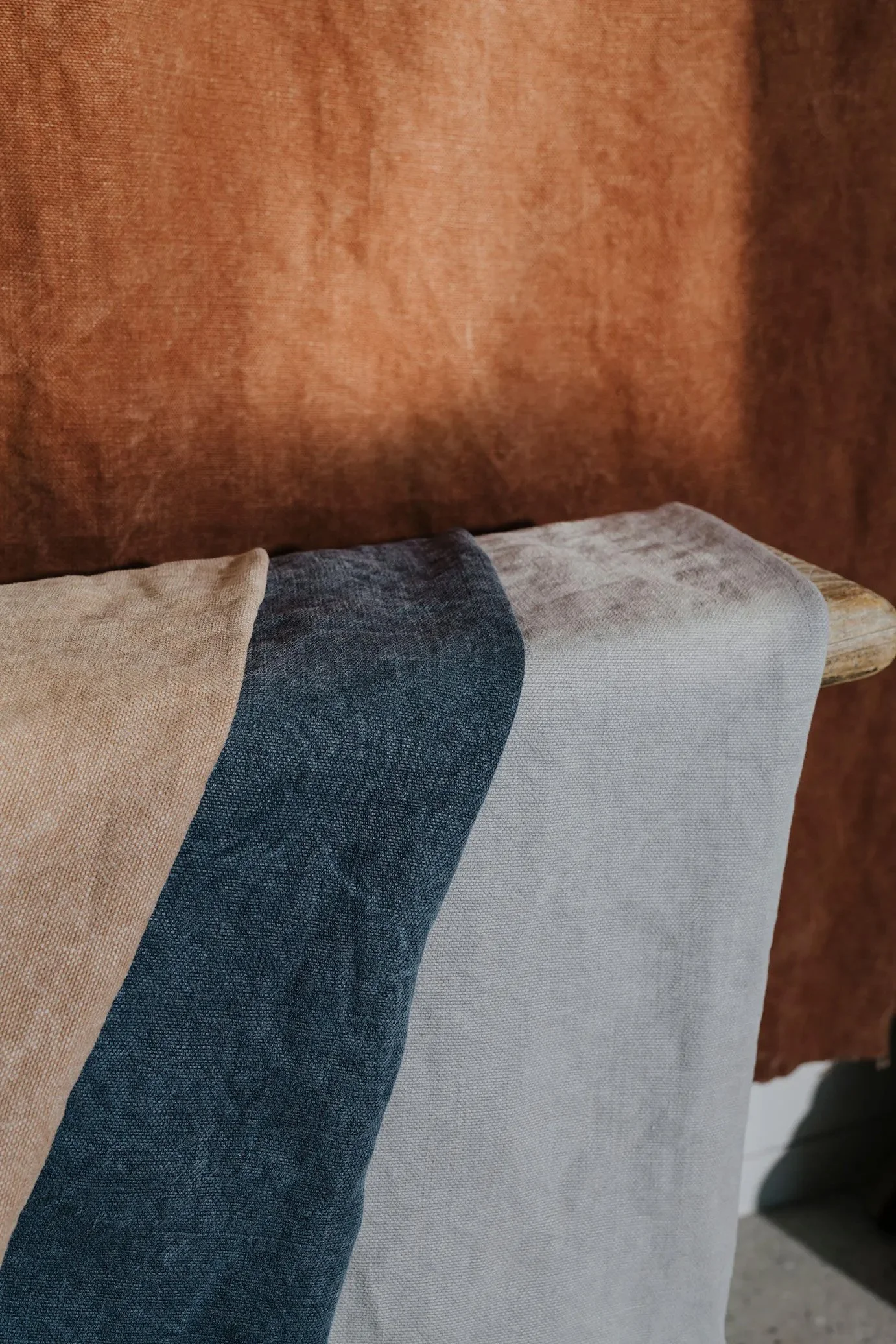 Close-up of a fabric-covered bench with beige, dark blue, and light gray fabrics, and a brown textured background.