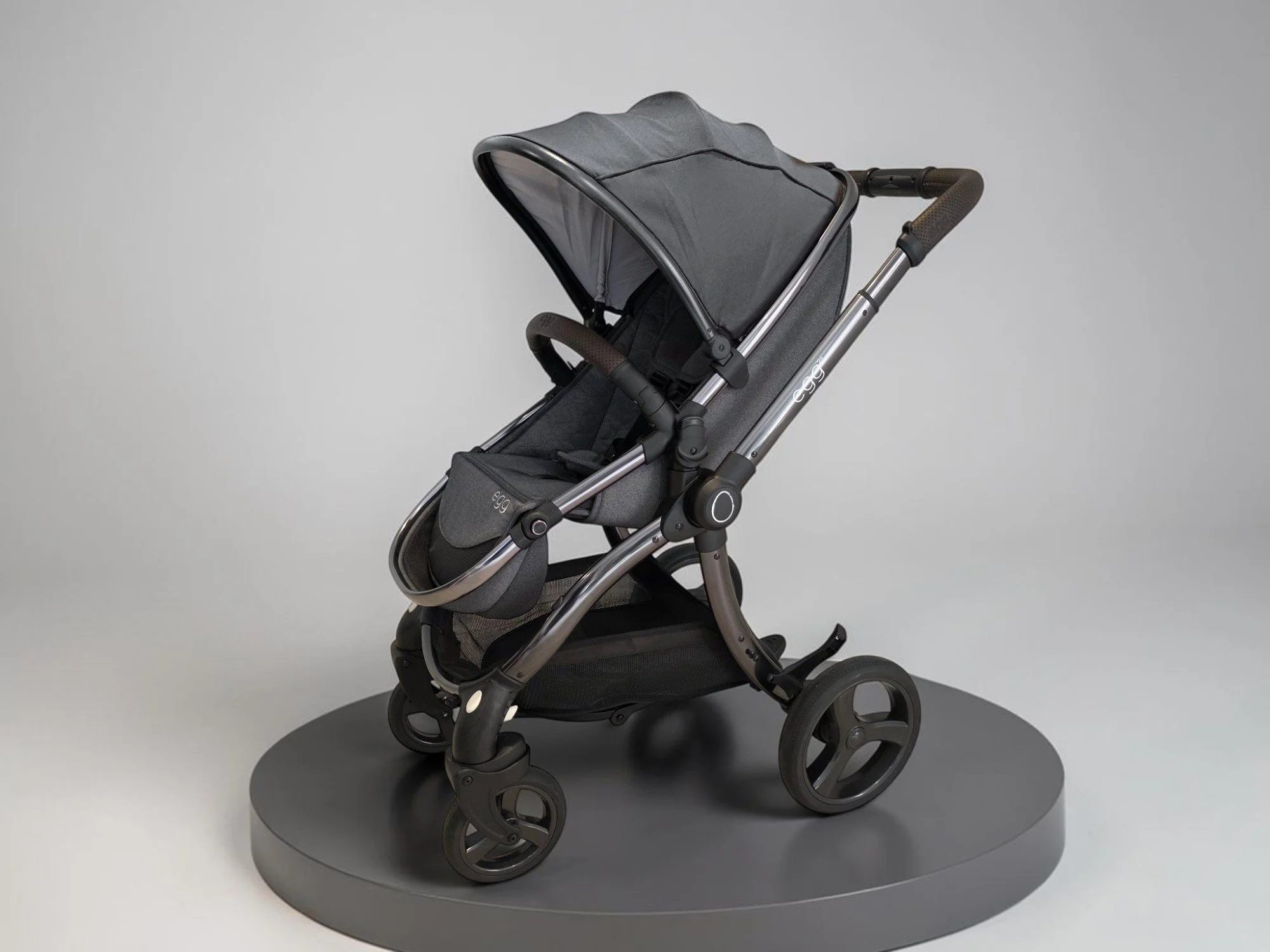 Egg stroller with grey canopy and seat on a circular display plinth.